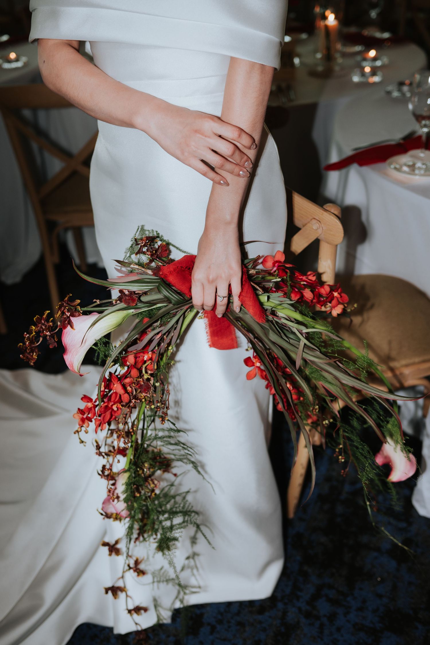 Elegant white wedding dress adorned with cascading red berries and greenery bouquet at indoor reception venue.