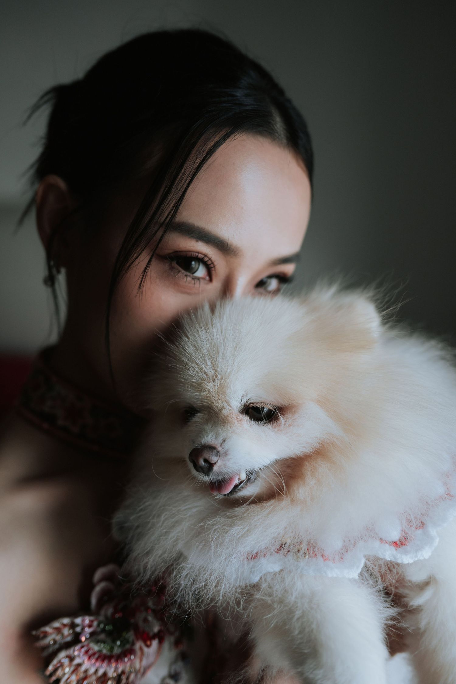 A young Asian woman holds a fluffy white Pomeranian dog close to her face, smiling warmly.