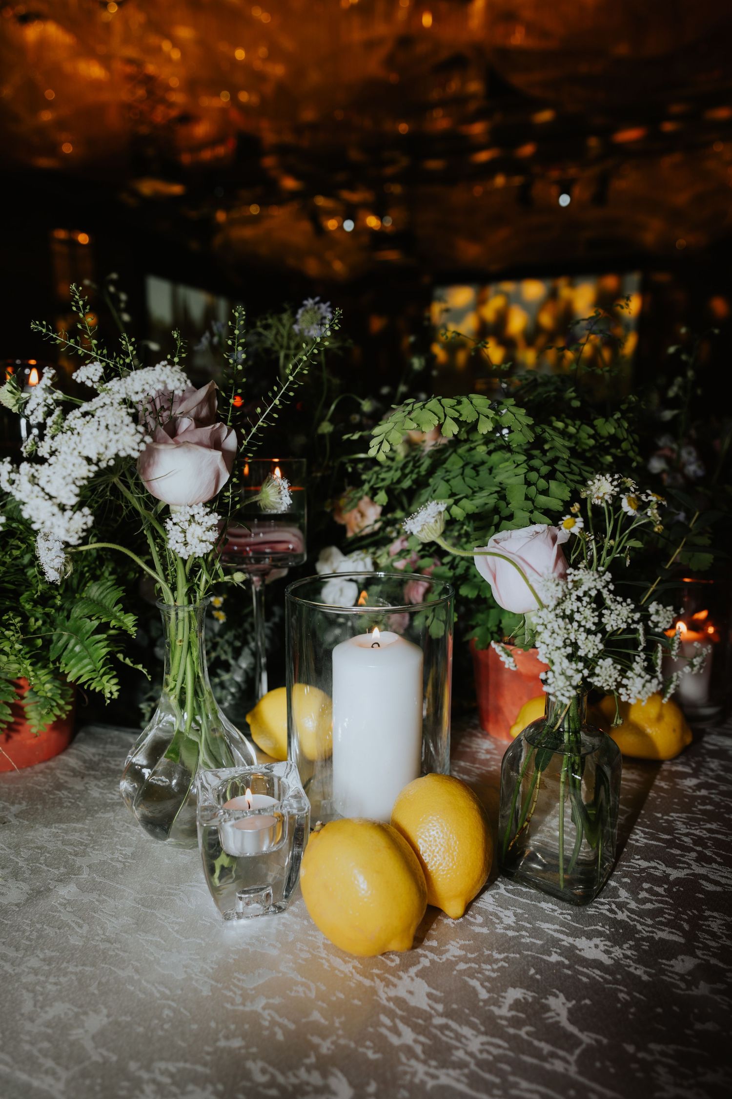 Rustic table setting with fresh lemons, white flowers in glass vases, and candles creating a warm ambiance.