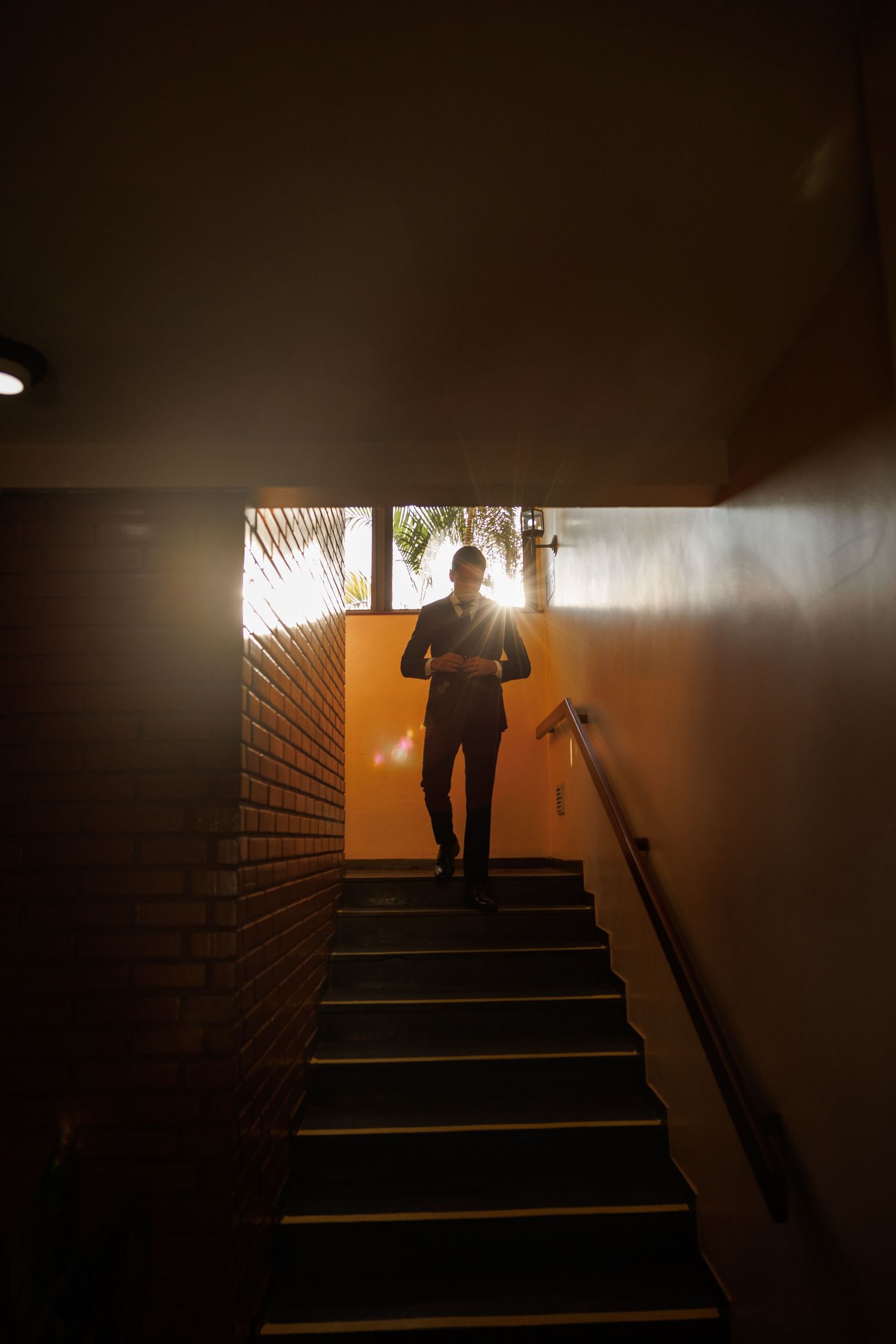 A silhouetted figure ascends stairs in a dramatically backlit corridor.