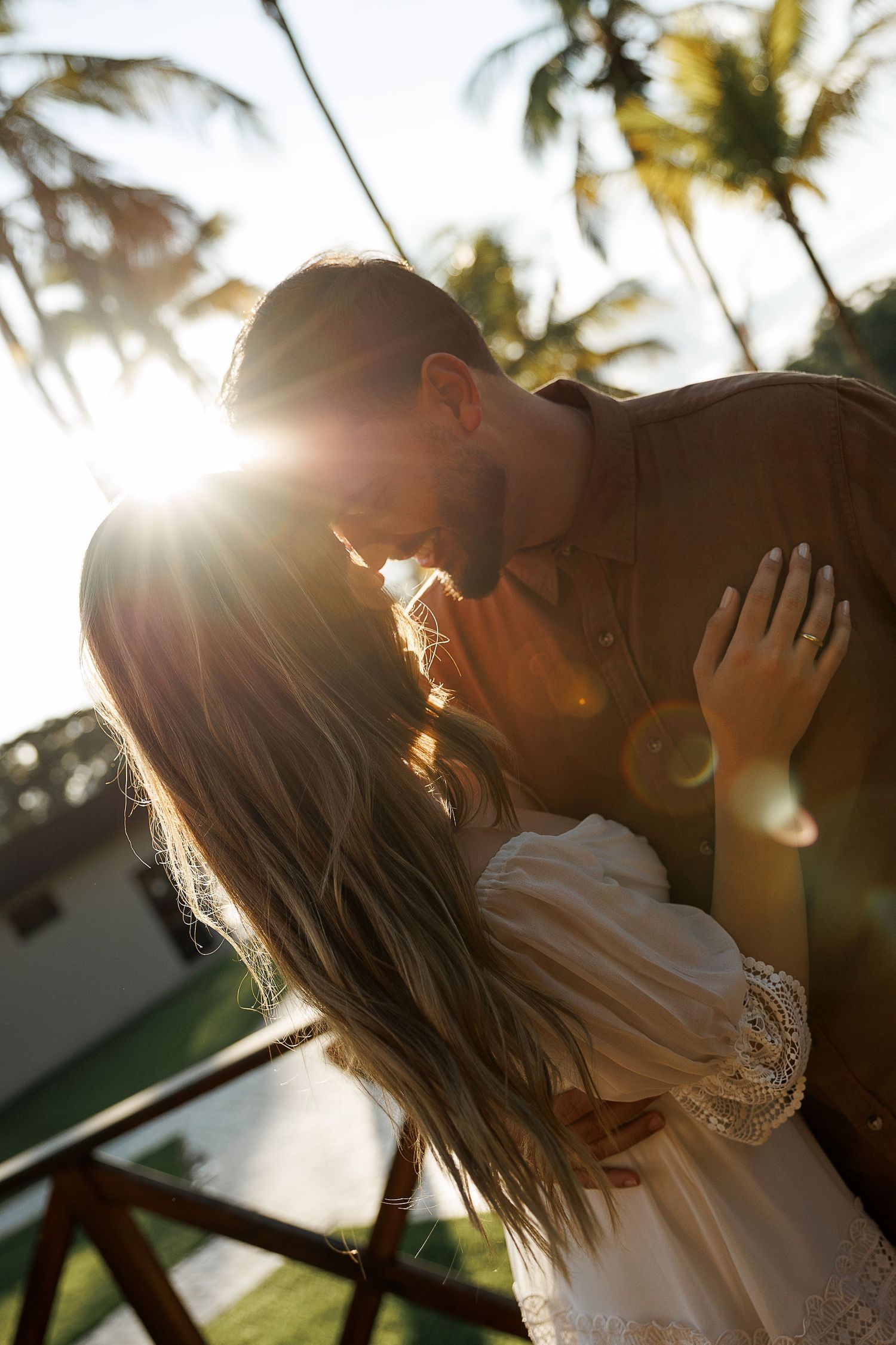 Romantic sunset photoshoot with palm trees and lens flare creating dreamy atmosphere.