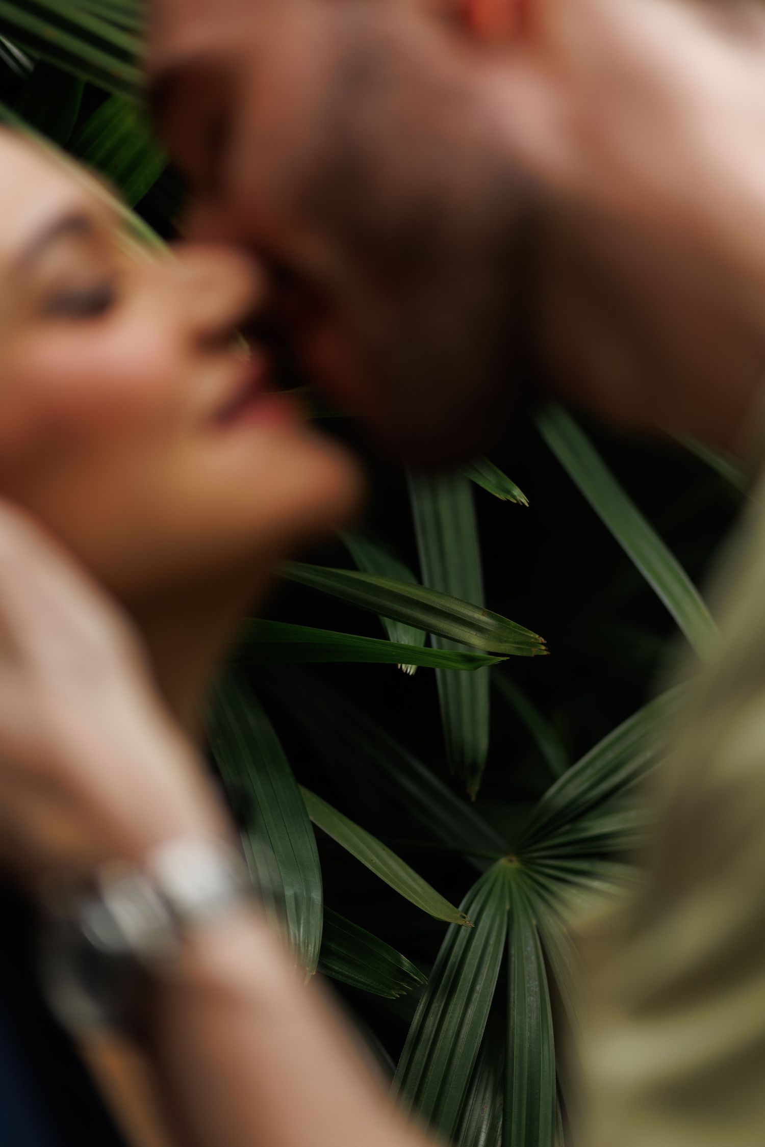 Intimate moment captured through palm leaves creating a natural frame.