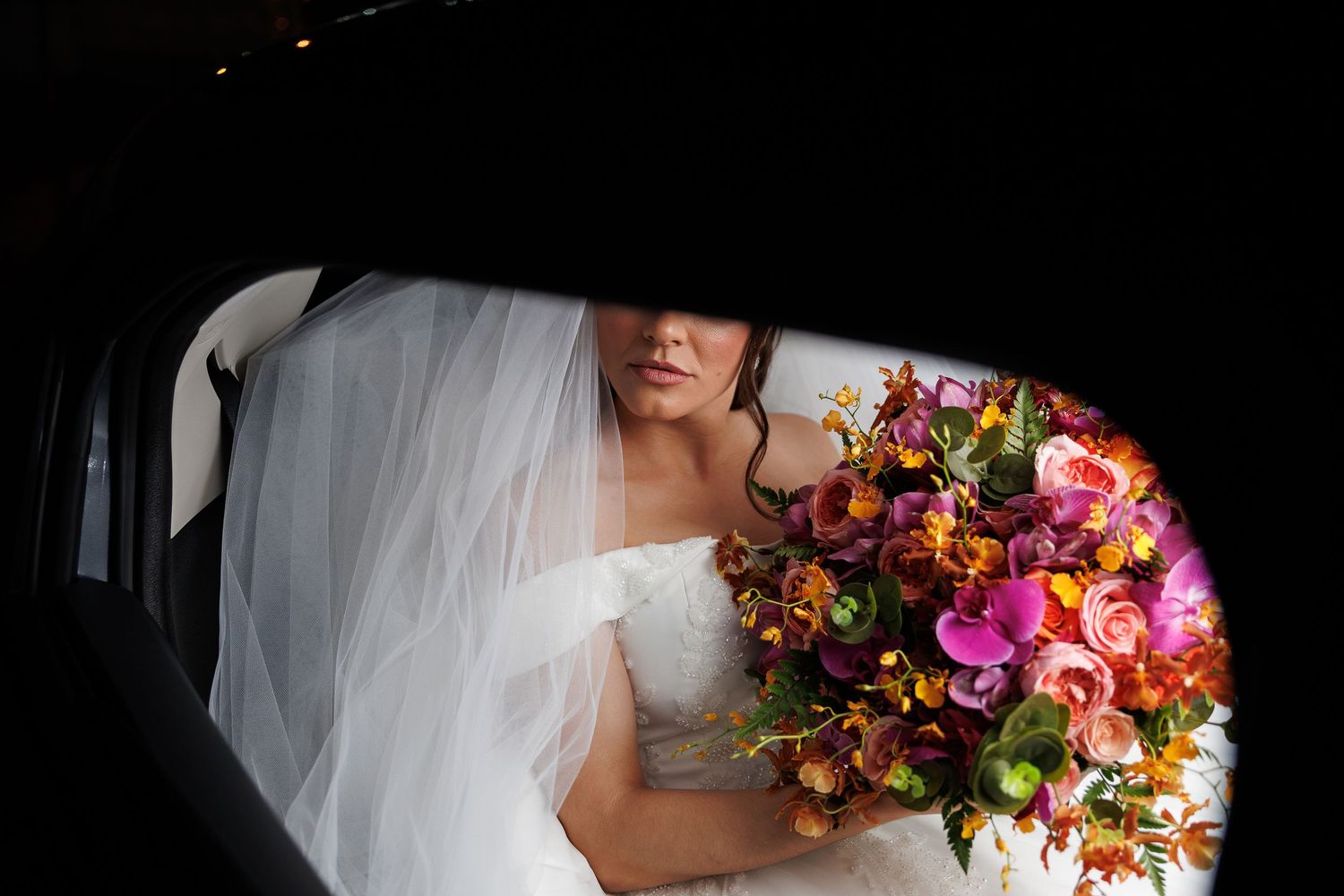 Vibrant colorful wedding bouquet with pink and orange flowers against a white bridal gown.
