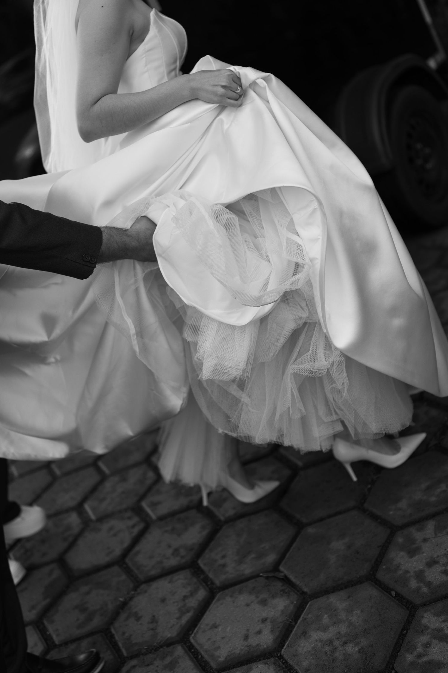 Black and white detail shot of a wedding dress flowing over cobblestone ground.