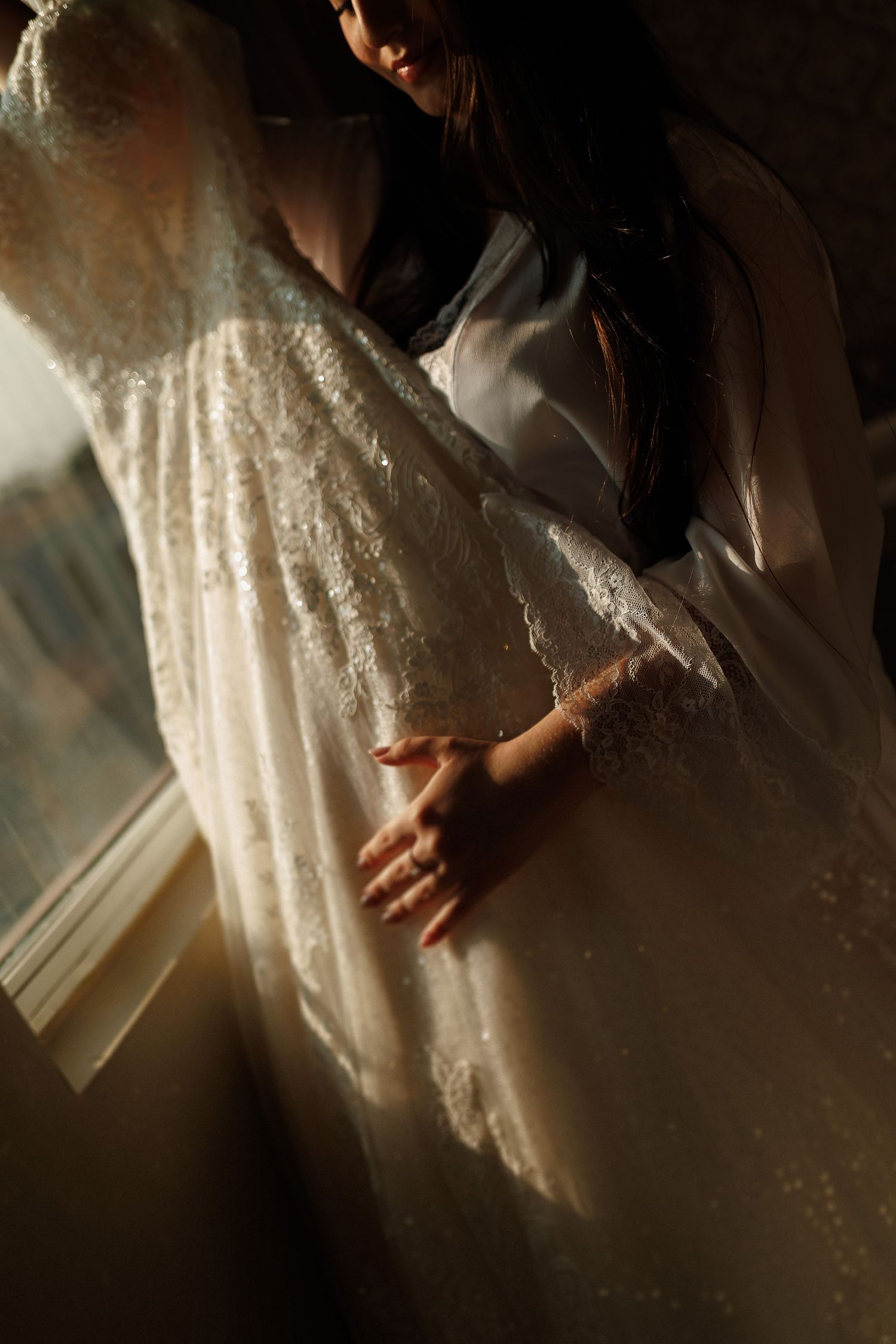 Close-up details of an ornate white lace wedding dress in dramatic lighting.