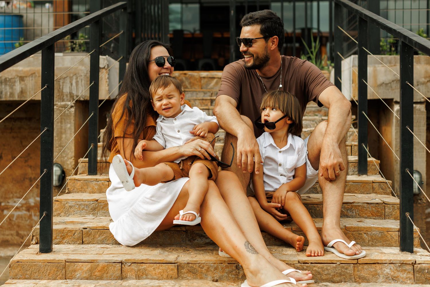 Family relaxing on outdoor steps in casual summer attire.