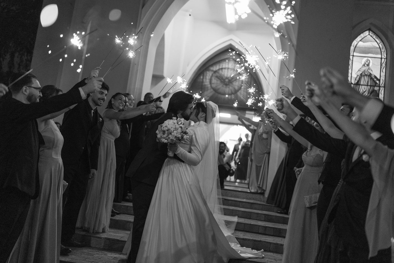 Black and white photo of wedding celebration in a church with dramatic lighting and arched architecture.