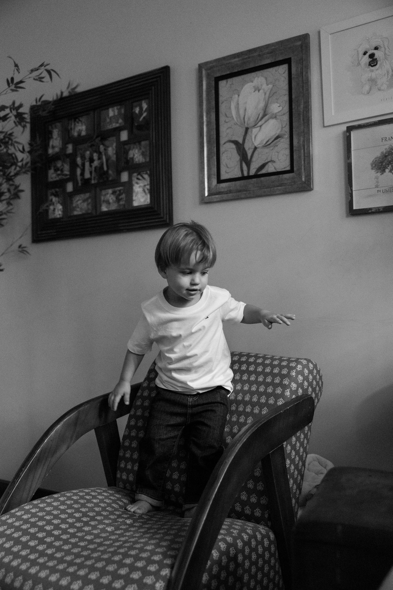 Child playing on a patterned couch in a room with framed artwork on the walls.