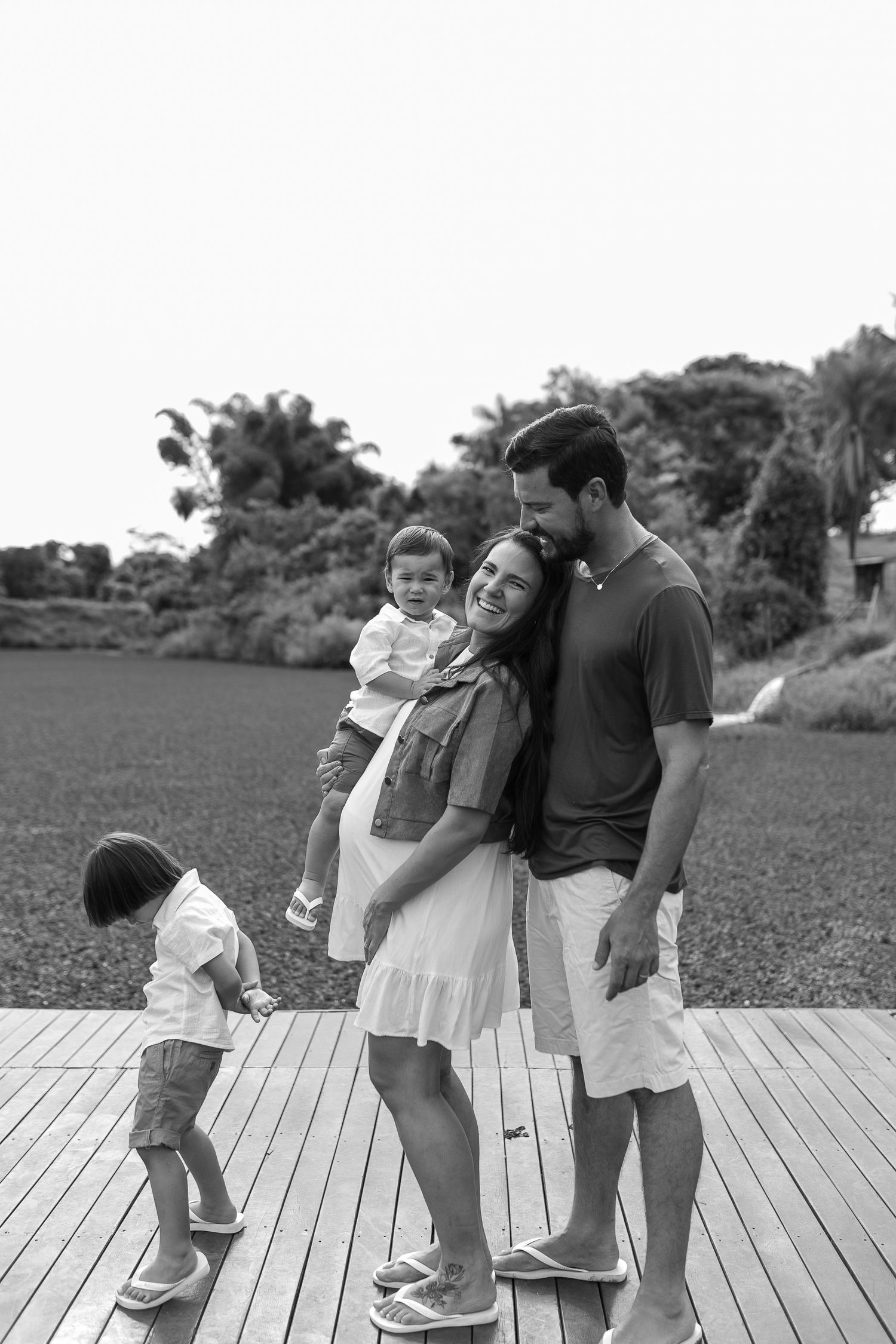 Family group poses playfully on wooden deck outdoors in black and white.
