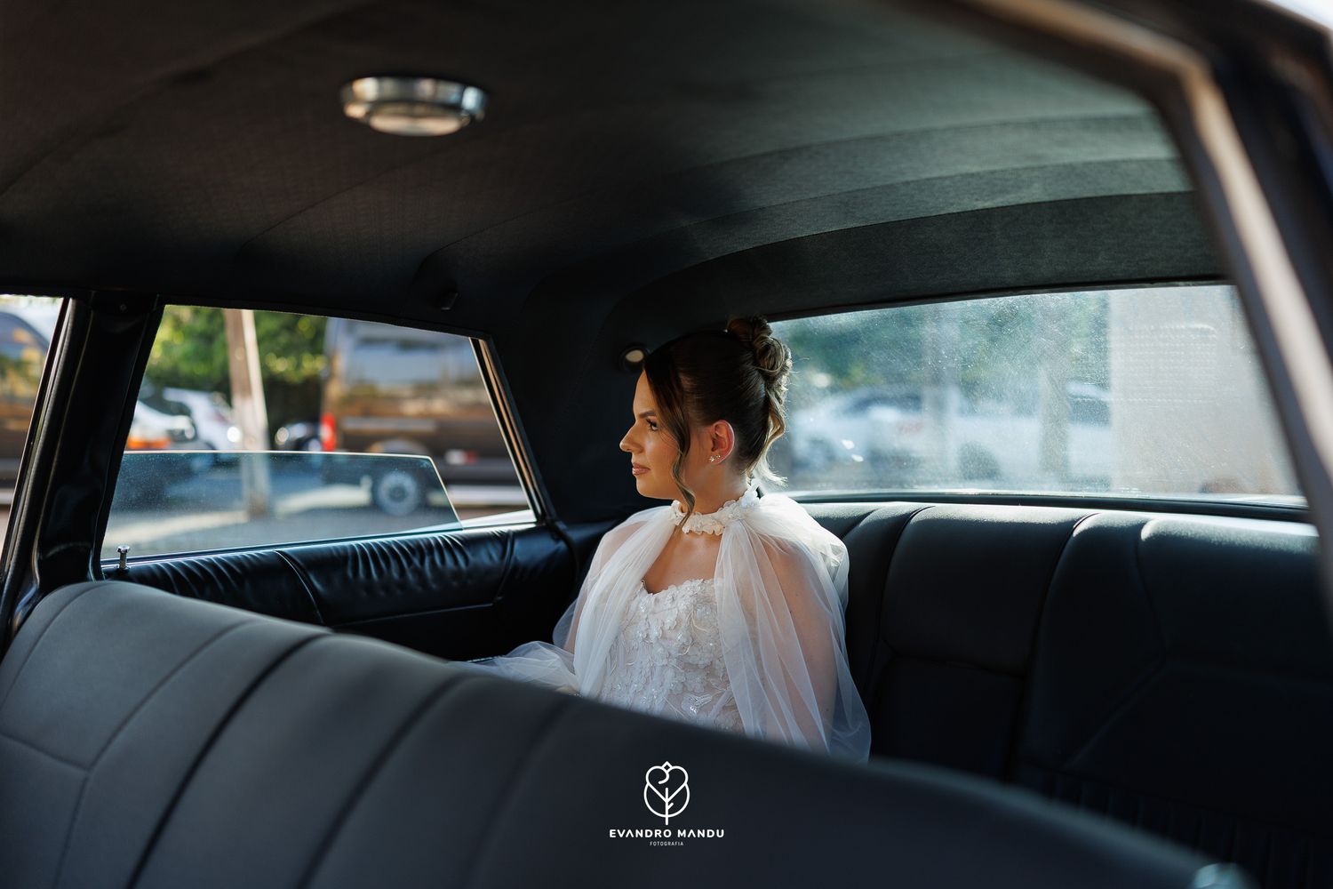 A bride sits in the backseat of a vintage car wearing a delicate white veil.