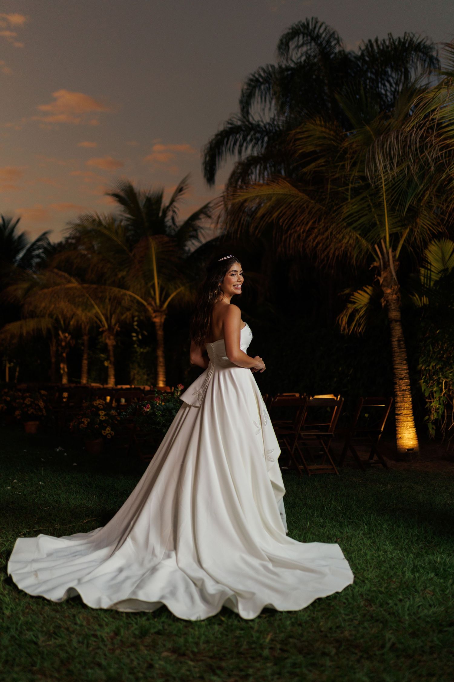 A dramatic evening portrait of a bride in a ballgown against illuminated palm trees.