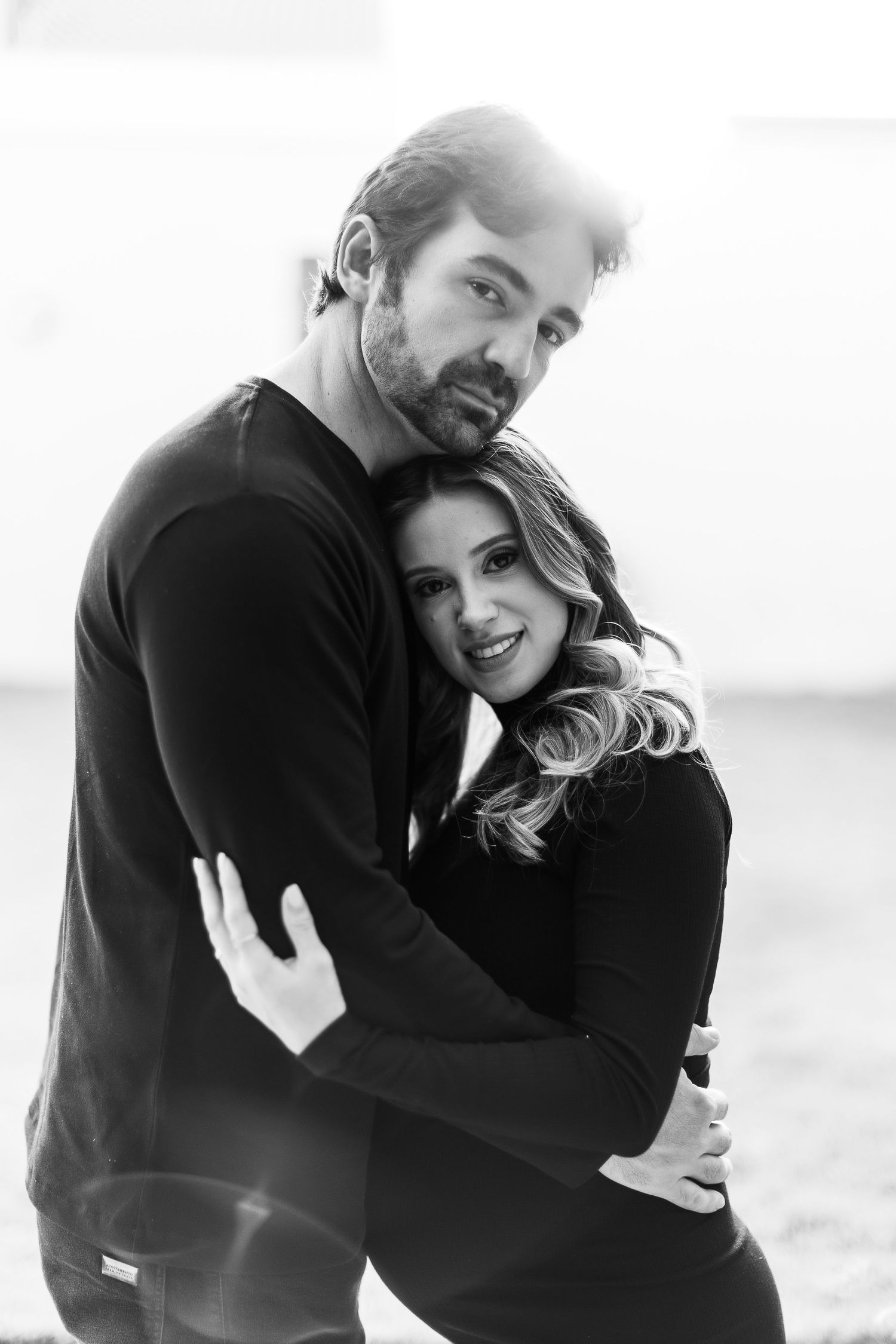 Black and white portrait of couple sharing tender embrace against bright background.