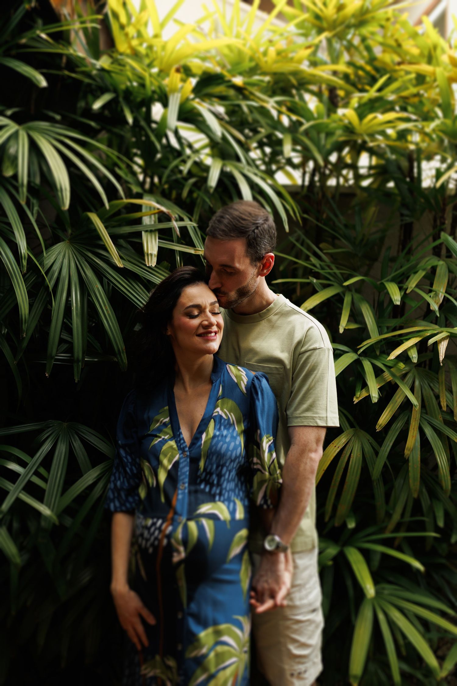 Romantic couple sharing tender moments among tropical plants and palm fronds.
