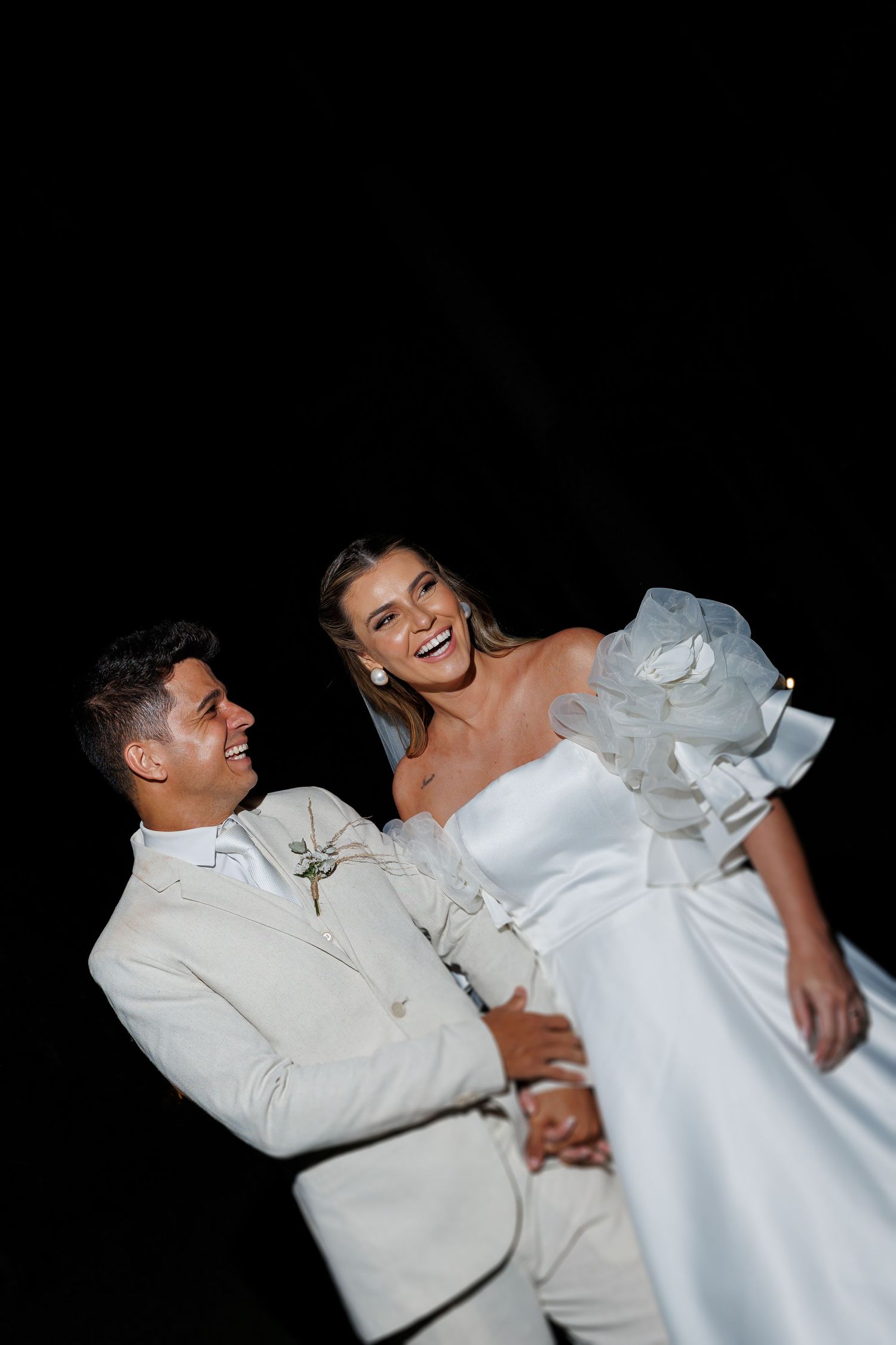 Wedding couple dancing and laughing together in matching white formal attire.