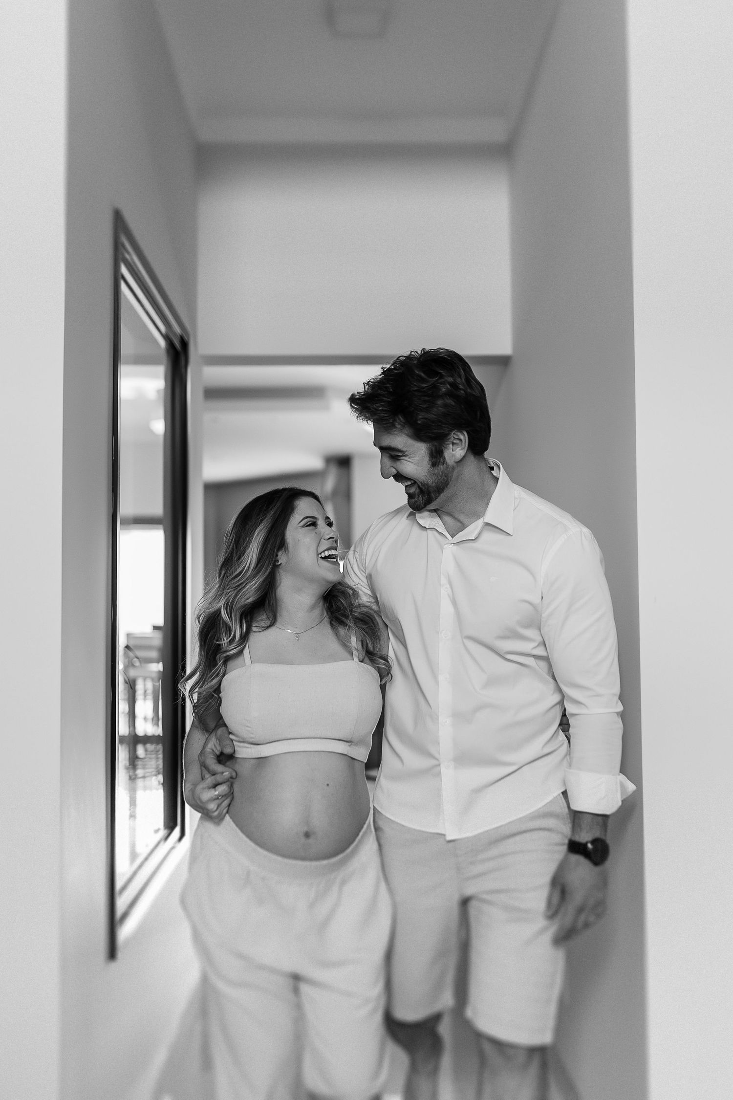 Couple in matching white outfits share intimate moment in bright hallway.