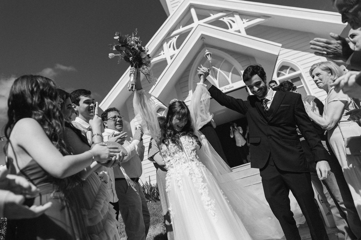 Wedding party celebrating under a white pergola structure with hands raised in joy.