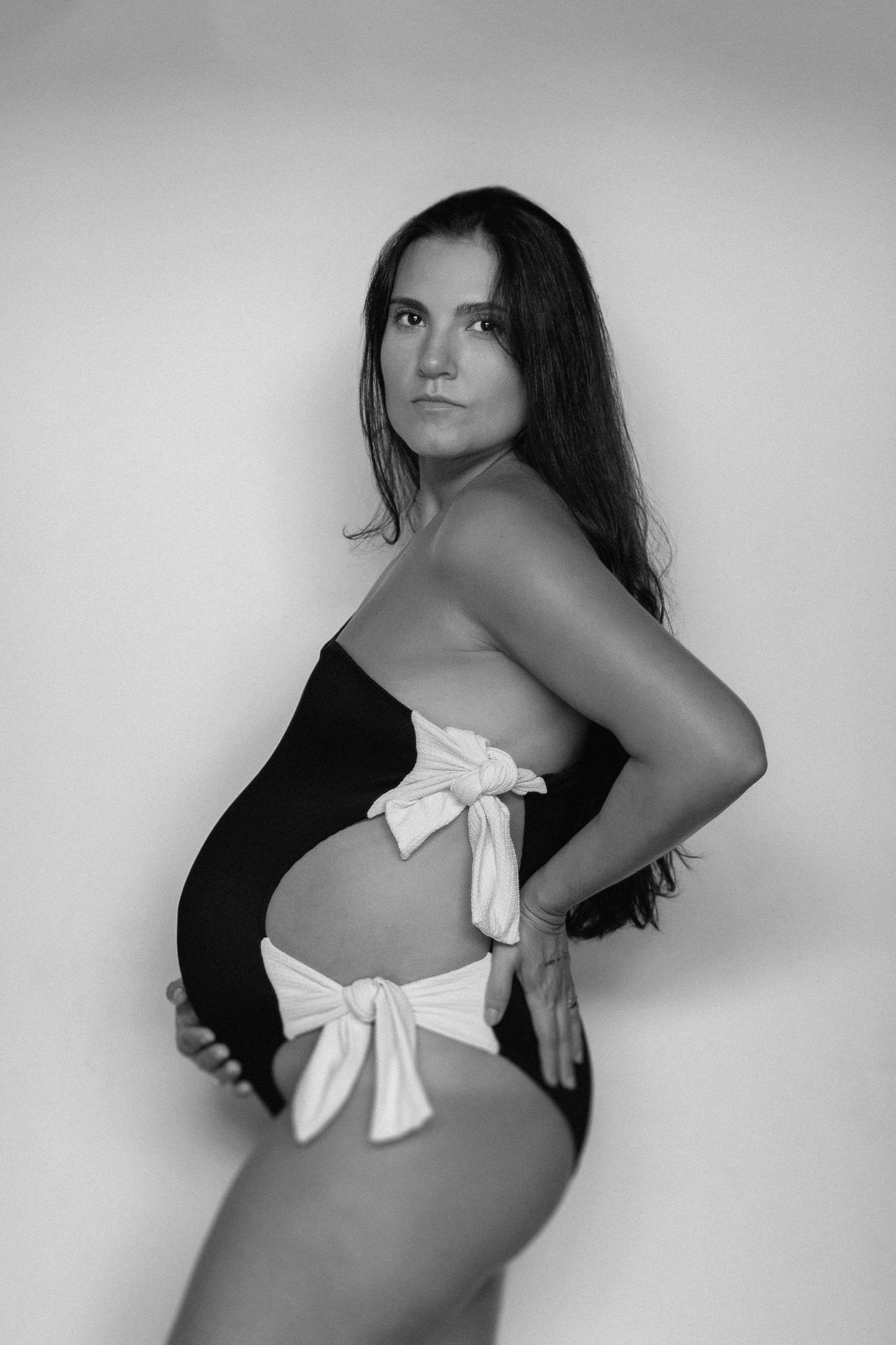 Black and white maternity photo series showing a white bow detail on clothing against a light background.