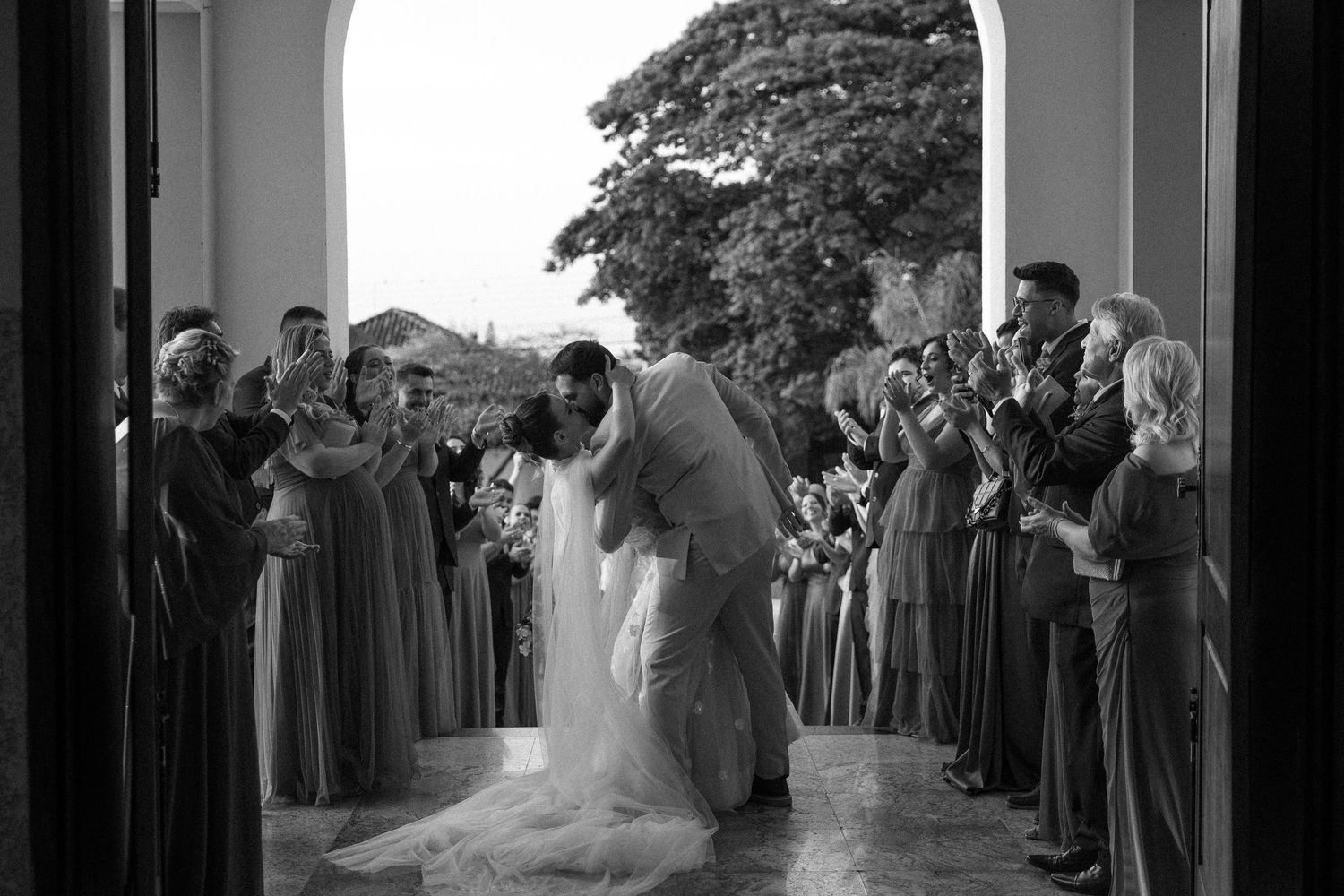 Wedding couple exits through church doorway as guests line the sides in black and white photography.