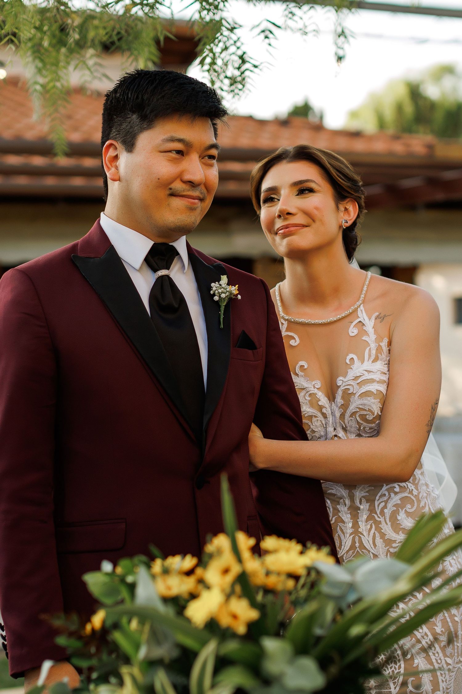 Couple shares intimate moment among yellow floral arrangements at outdoor reception.