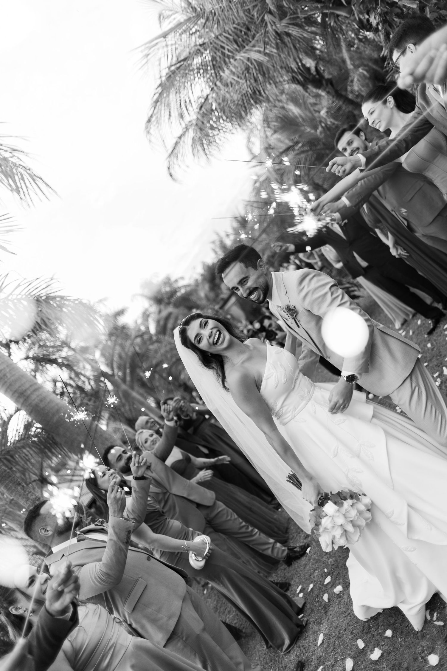 Wedding guests form a circle during an outdoor celebration with palm trees in the background.