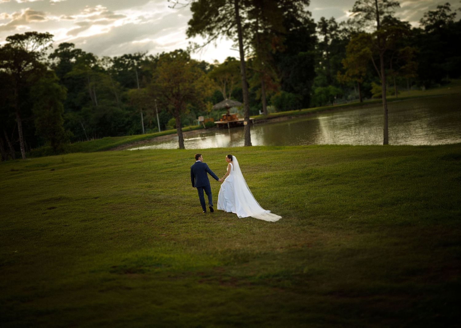 Wedding couple stands in silhouette against a dramatic sunset sky in a scenic outdoor setting.