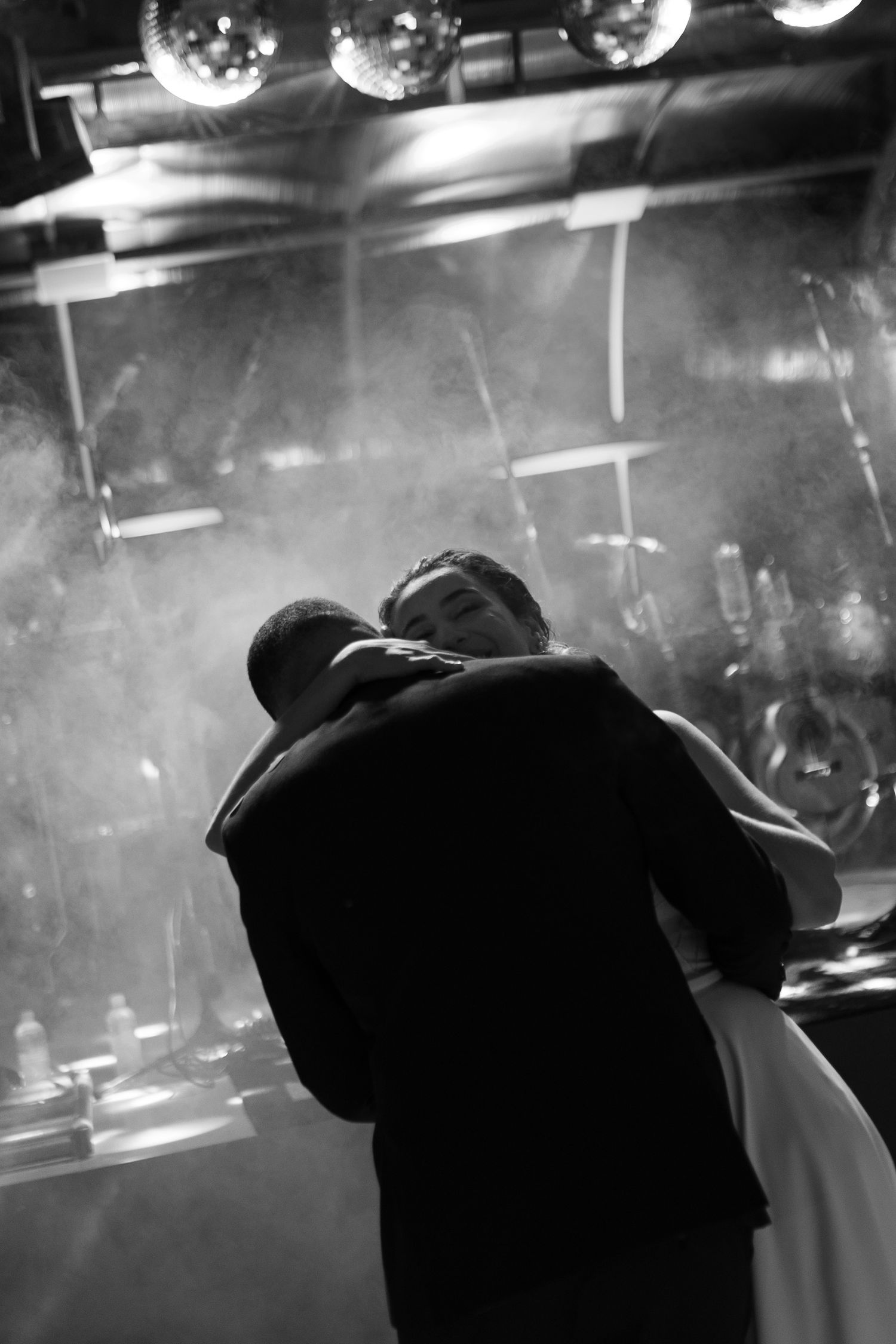 Silhouetted couple dancing under disco balls in a dark reception venue.