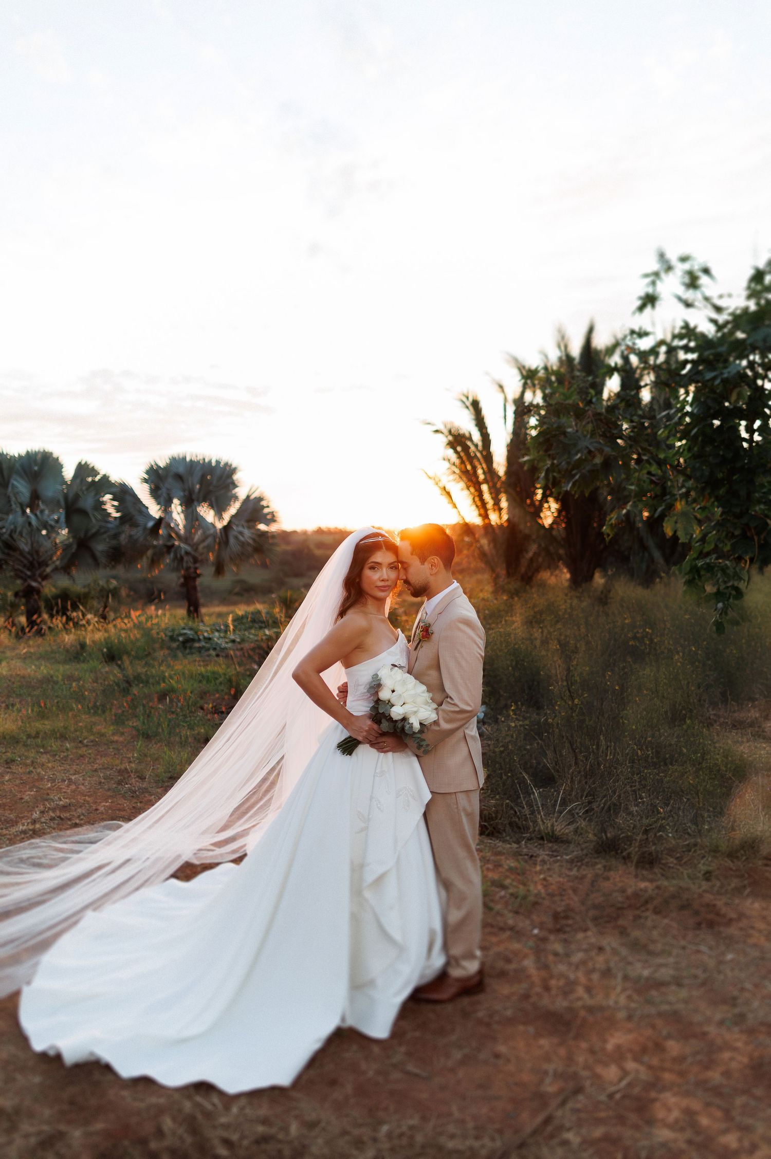 A couple shares a romantic moment at sunset with a flowing wedding dress train.