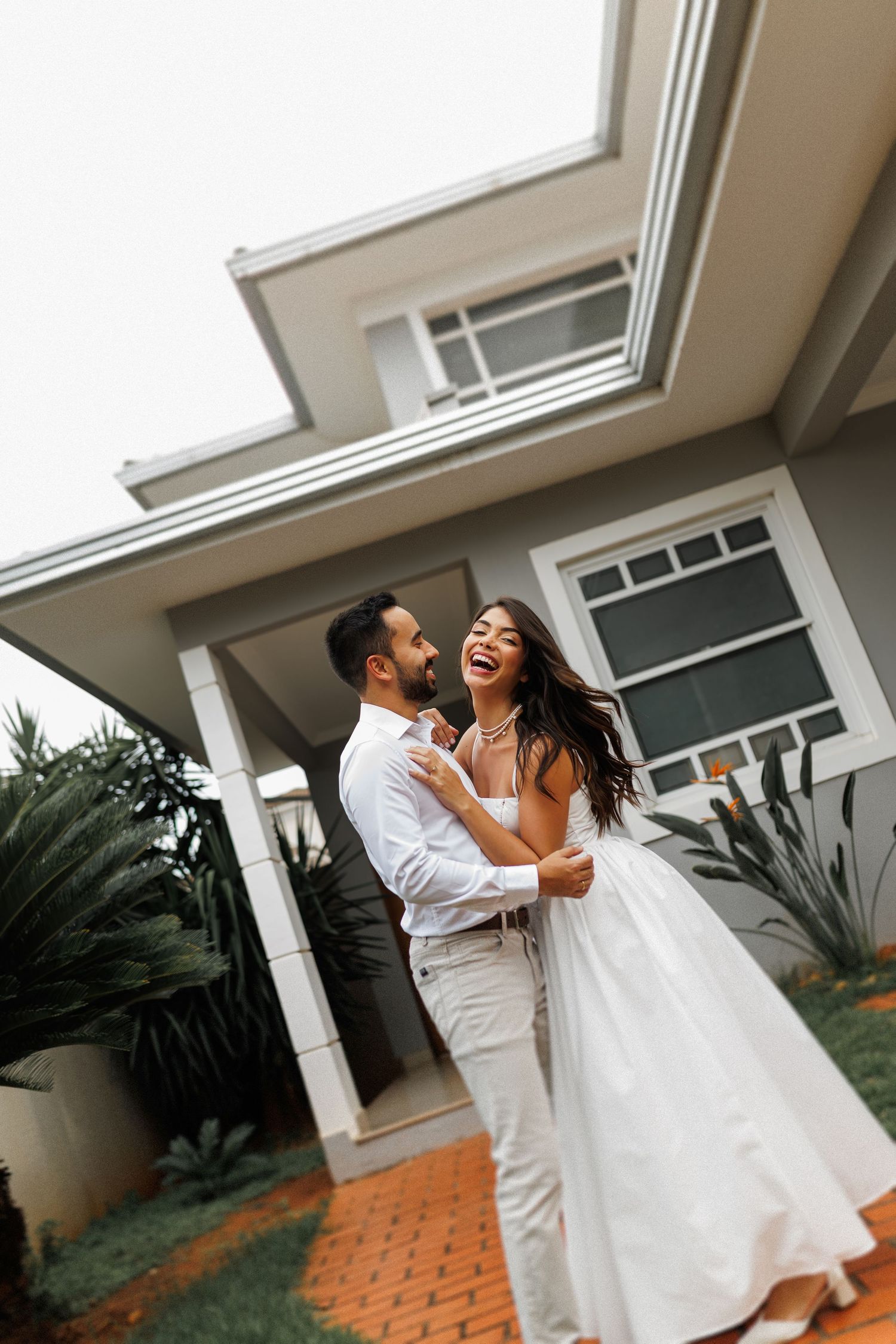 Couple in white sharing joyful moments outside a modern house.