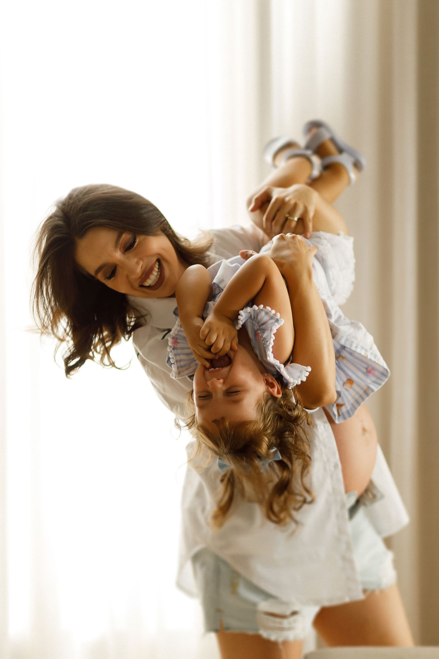 Mother and child share playful moments in white lace during indoor photoshoot.