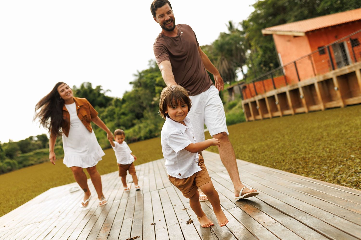 Casual outdoor family photoshoot on wooden deck with orange building in background.
