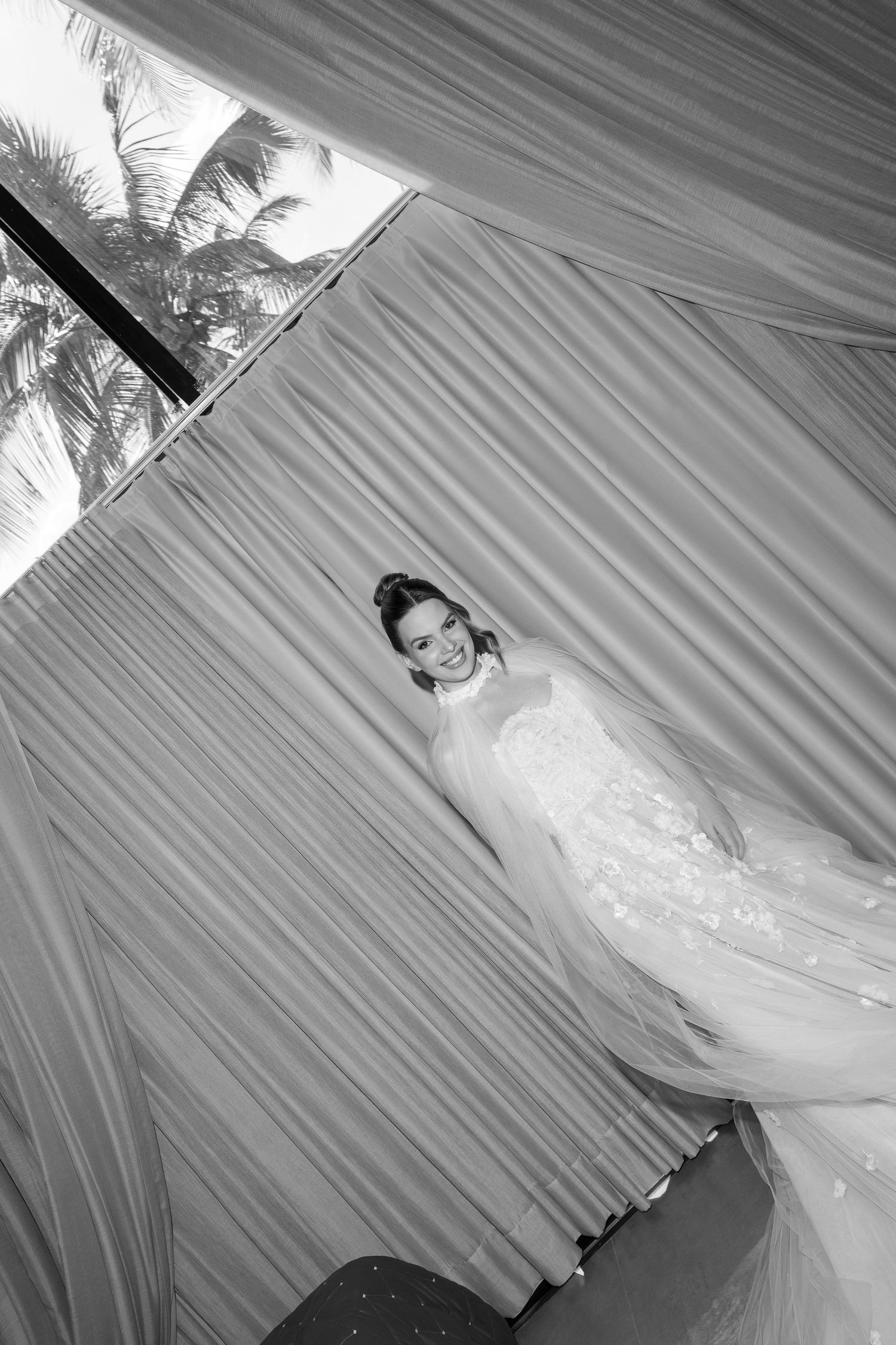 Black and white wedding dress photo with dramatic fabric draping and palm trees visible.