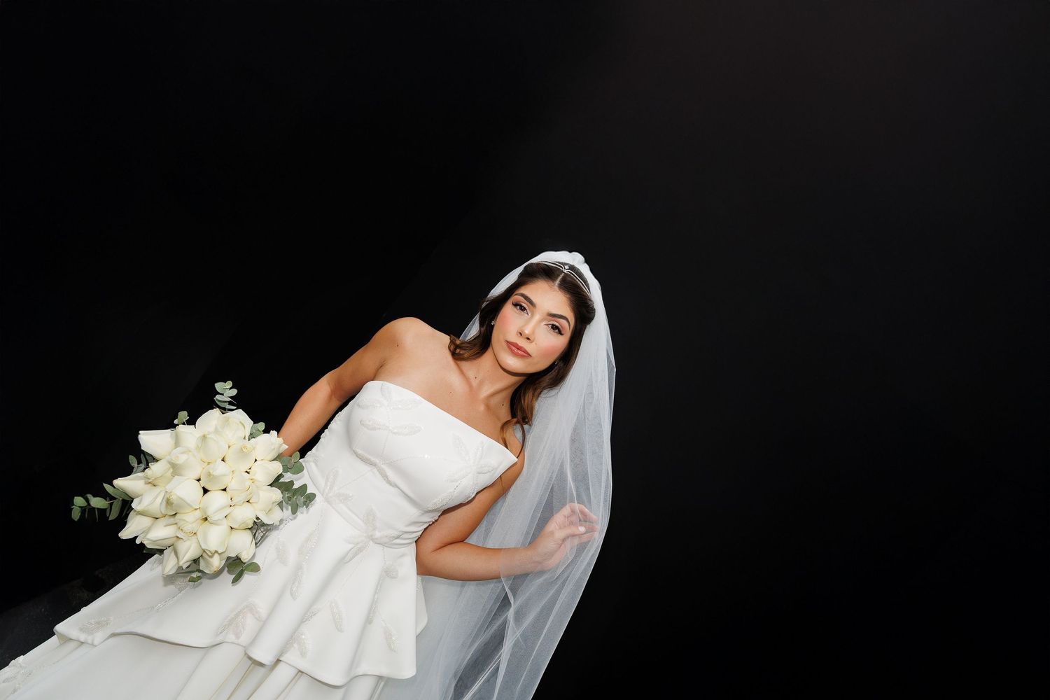 A bride in a strapless white gown poses against a dark background with classic elegance.