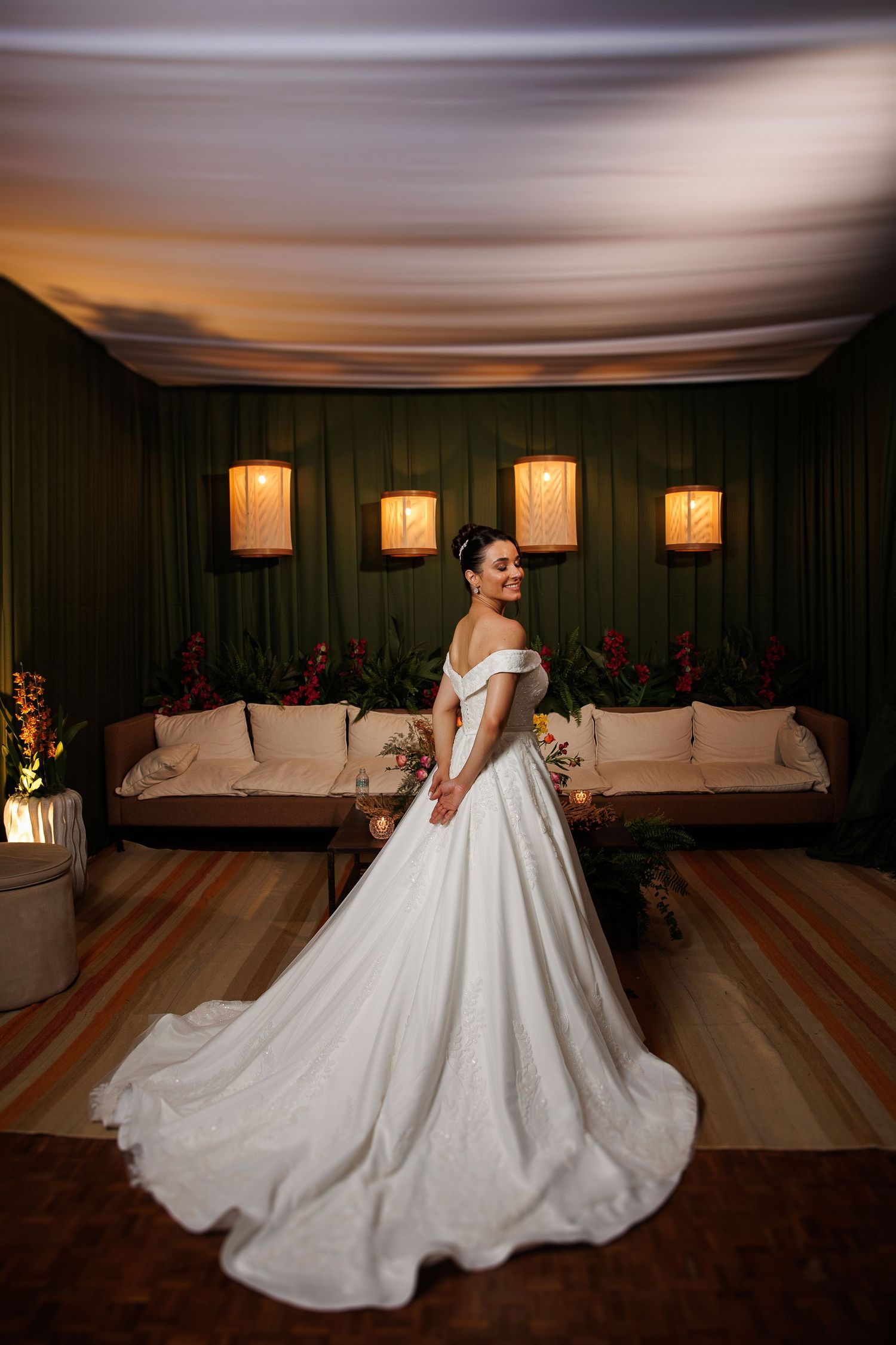 Elegant bride in flowing ballgown posing in a warmly lit room with decorative wall sconces.