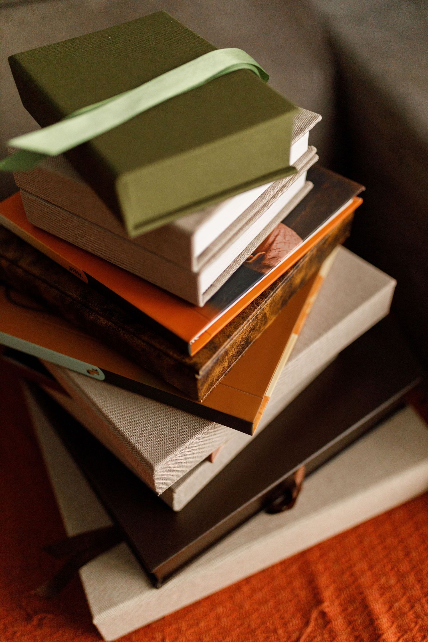 Stack of hardcover books in earth tones on an orange textured surface.