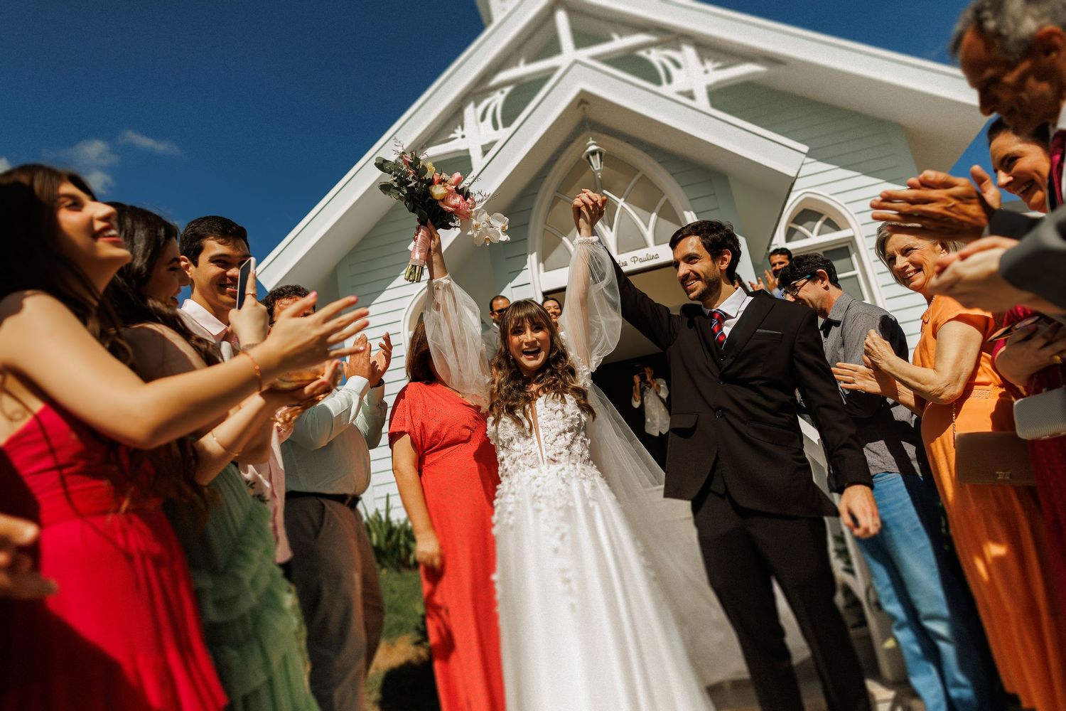 Wedding celebration outside white chapel with guests in colorful attire.