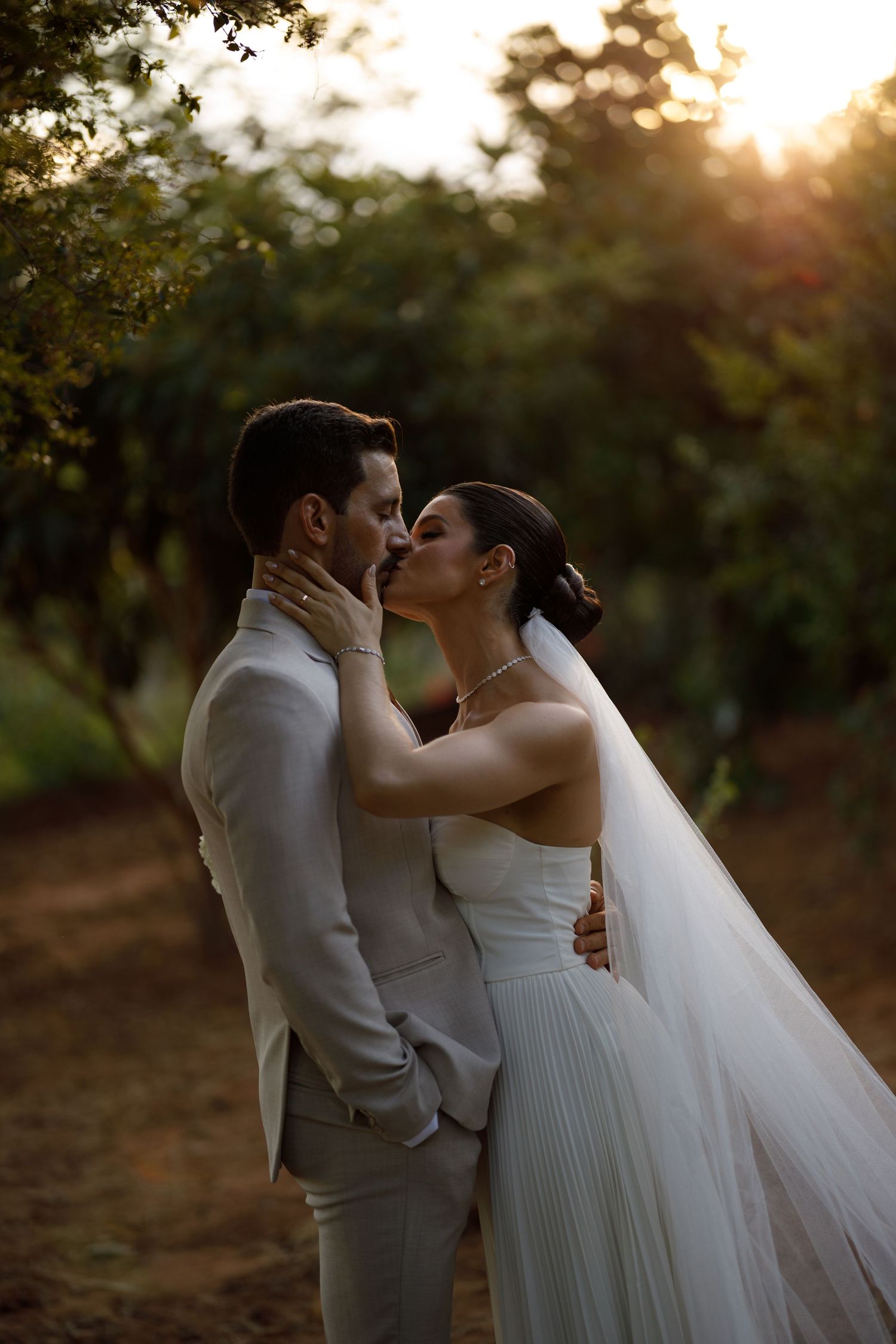 A romantic sunset wedding portrait shows a couple sharing a tender kiss in a golden-lit outdoor setting.