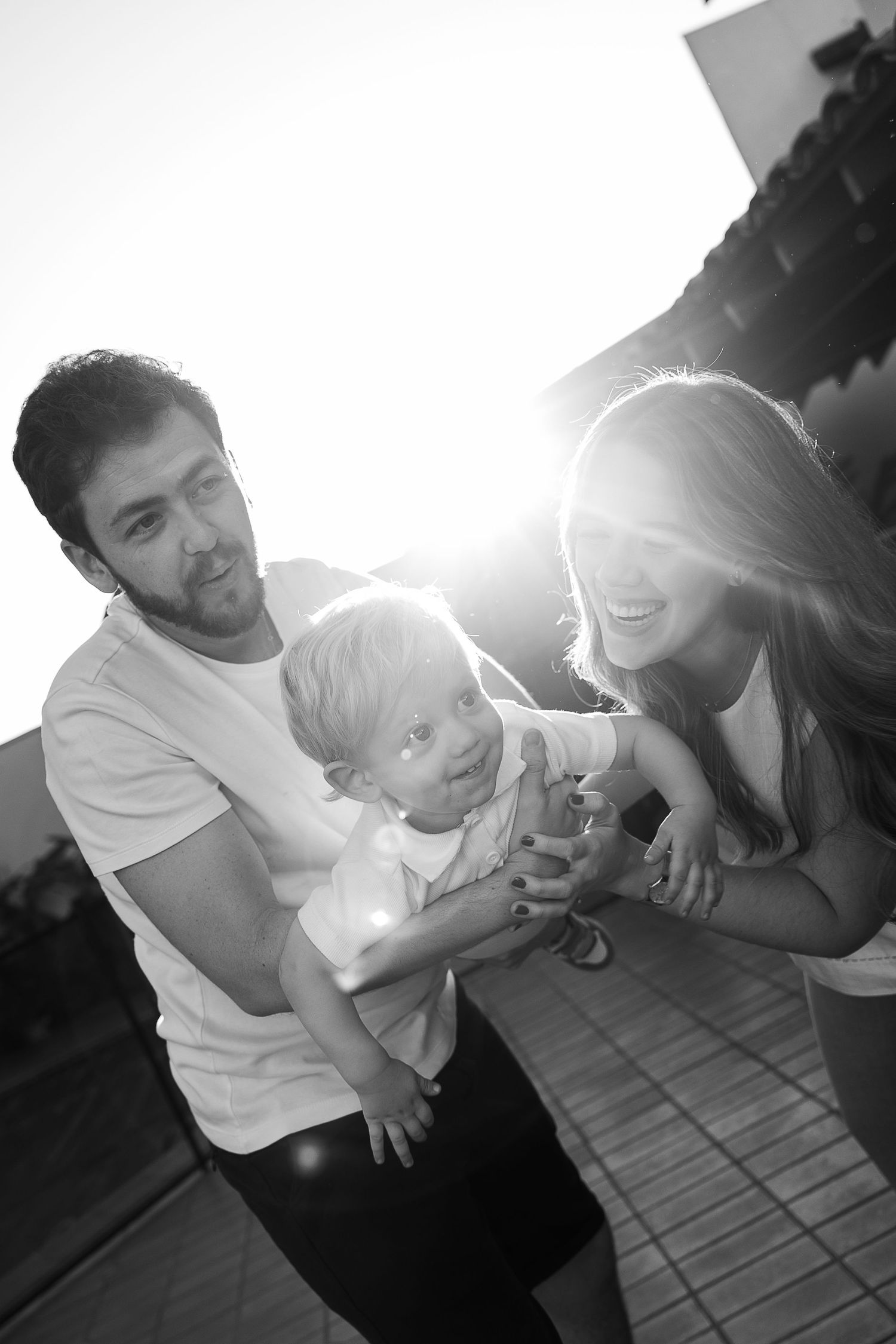 Black and white photo series showing playful family moments on a wooden deck.