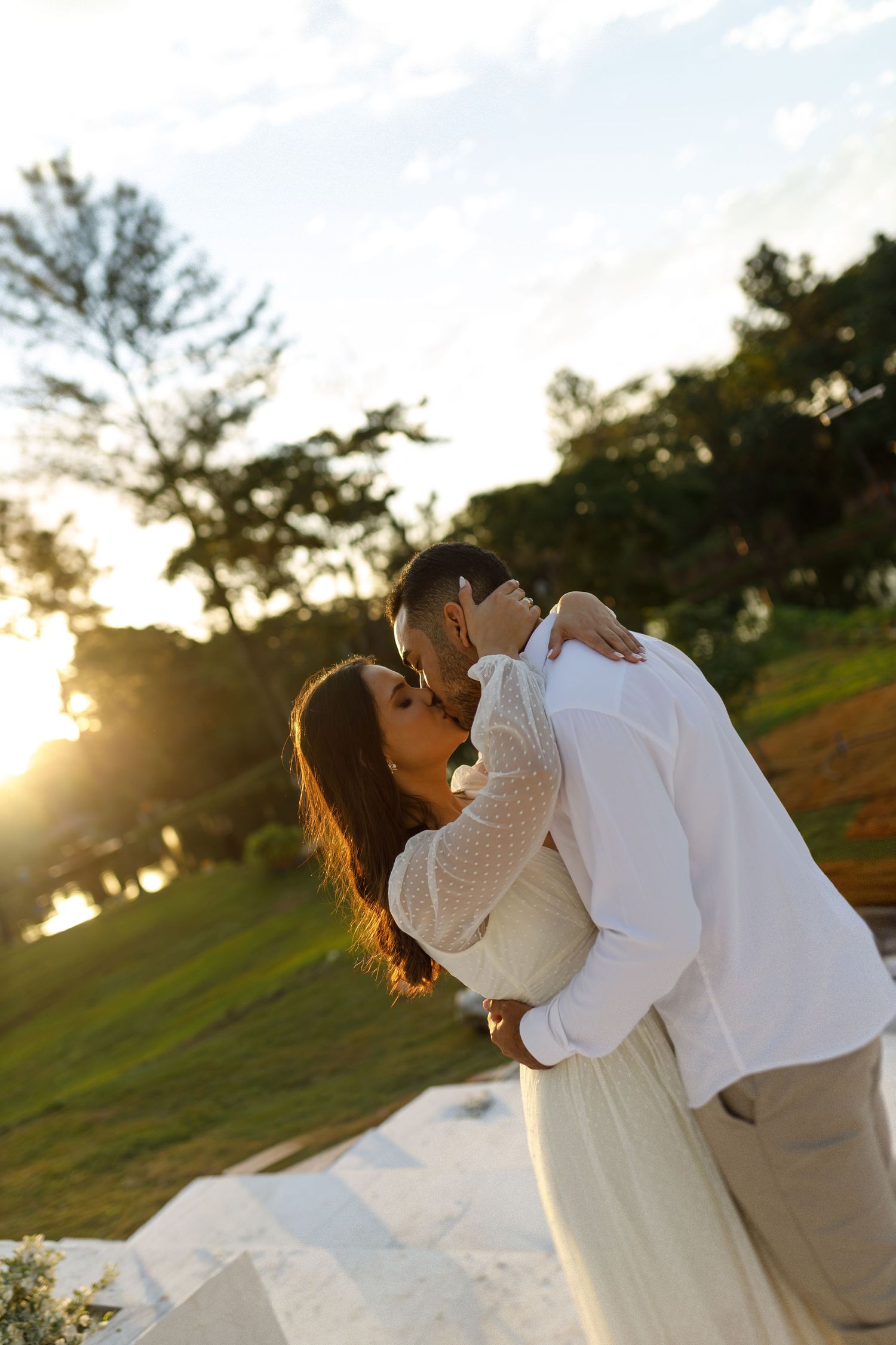 Romantic couple embracing during golden hour sunset in an outdoor setting with palm trees in the background.
