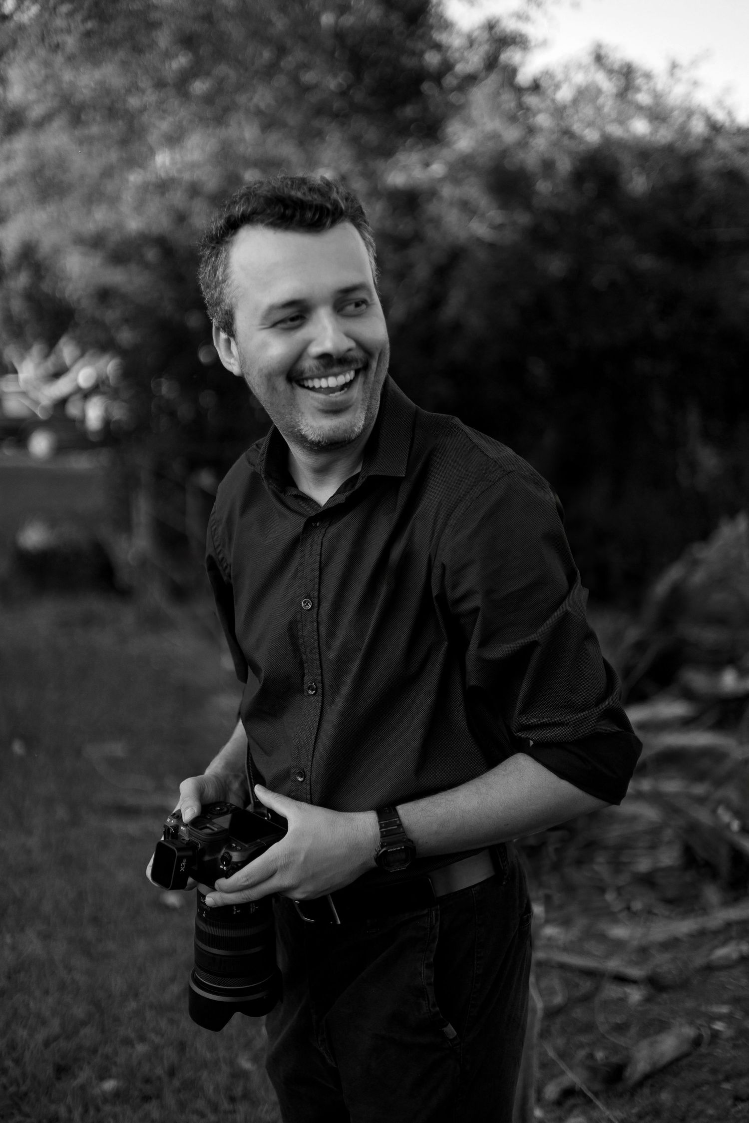 Black and white portrait of a photographer laughing while holding camera equipment.