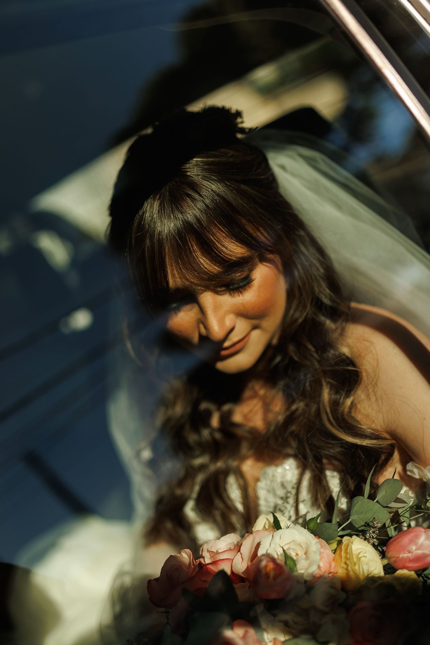 A bride poses with flowers in a romantic car window portrait series.