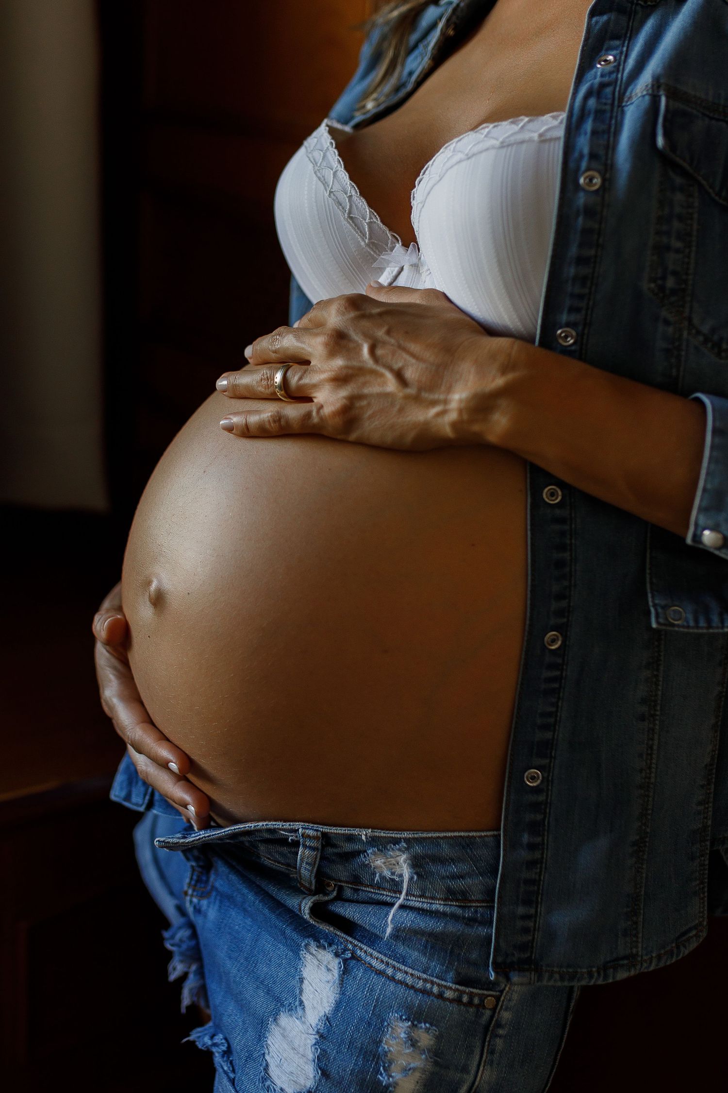 Close-up series of a pregnant belly in denim overalls against a dark background.