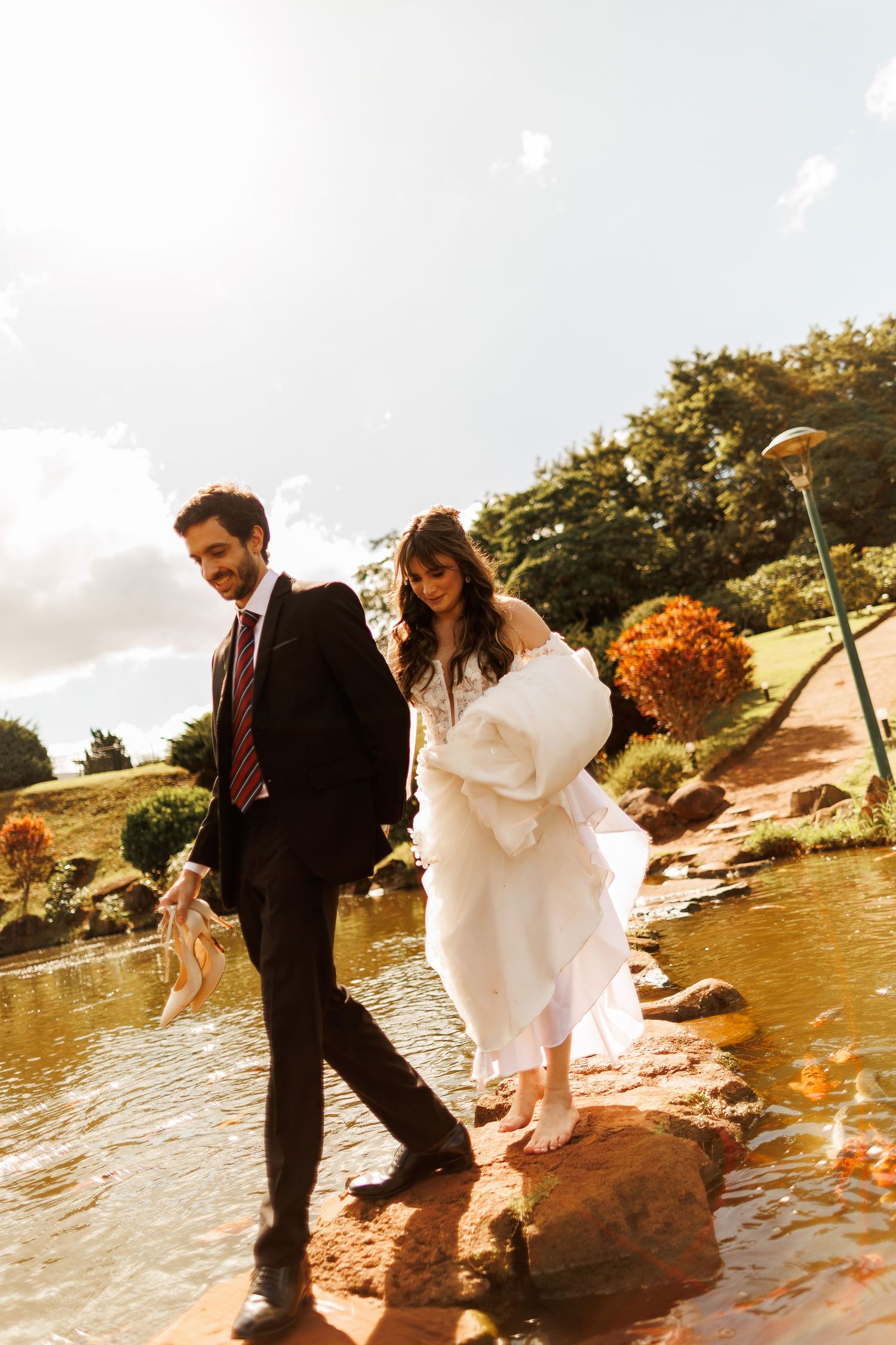 Playful wedding couple splashing and posing by a lakeside at sunset.