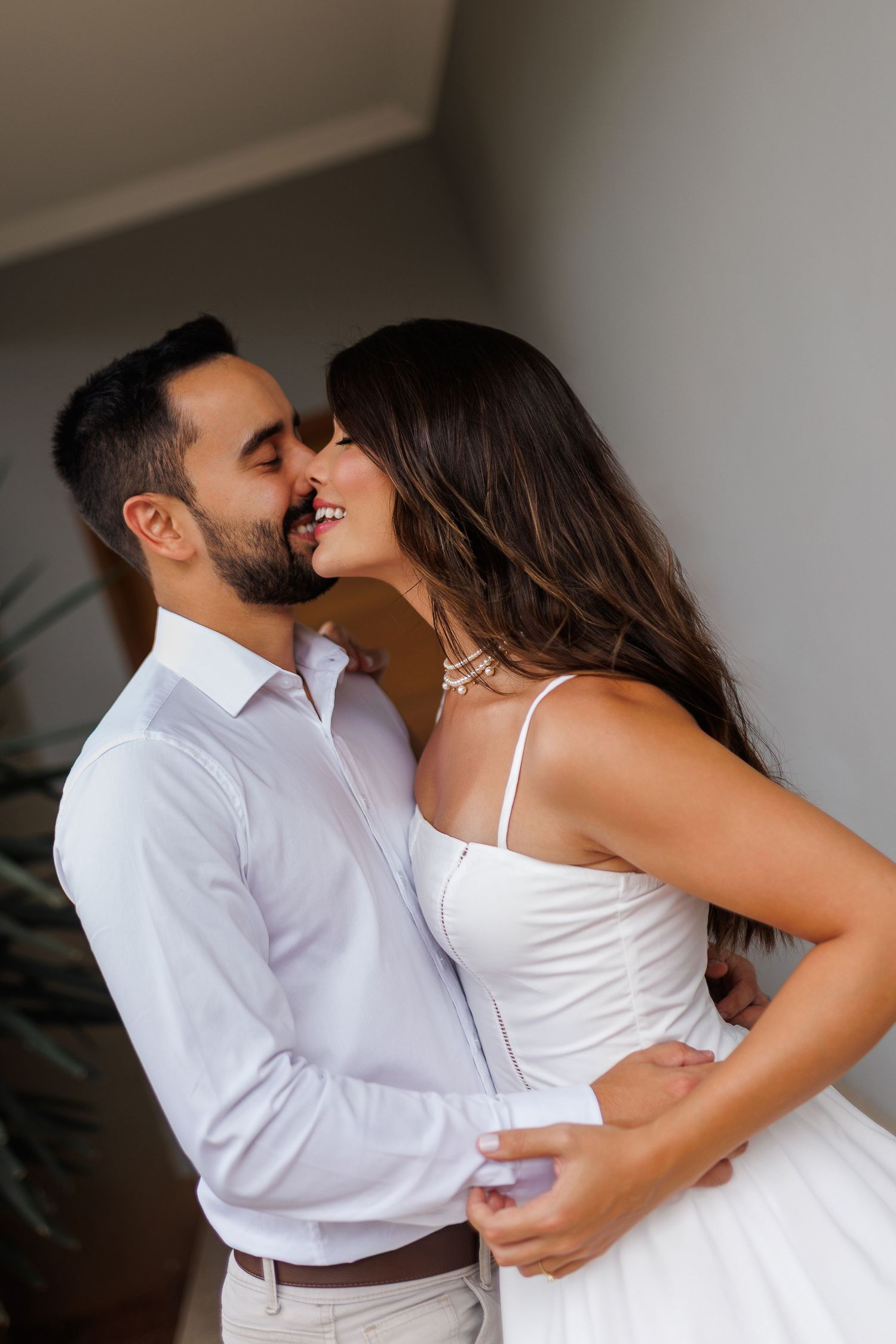 Intimate portrait of a couple in white clothing against an indoor backdrop.