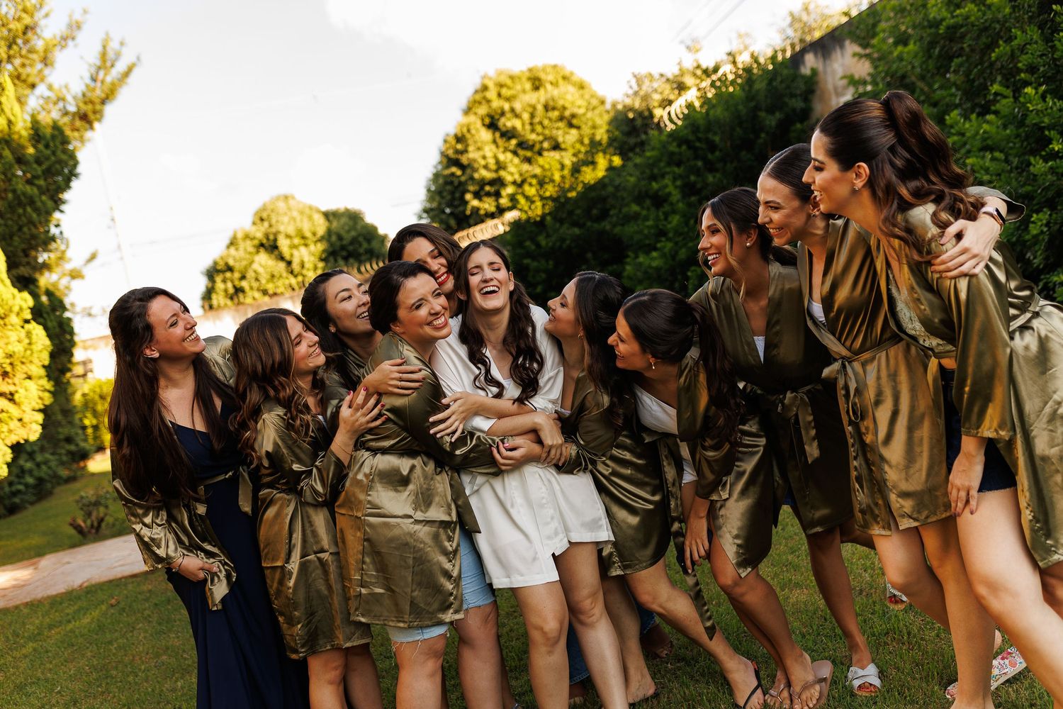 Group of bridesmaids in brown dresses posing together outdoors in golden sunlight.