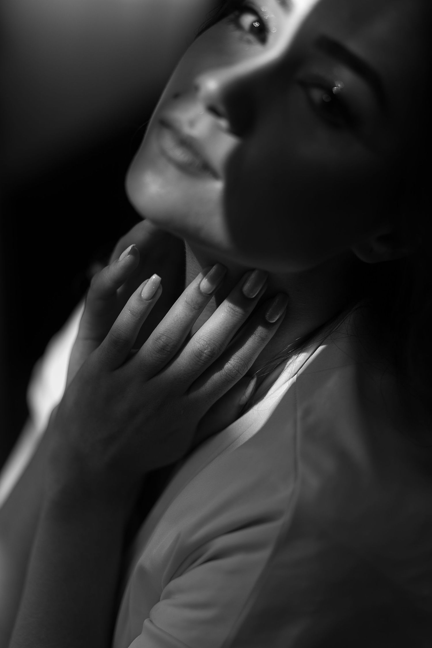 Artistic black and white close-up of hands touching face in dramatic lighting.