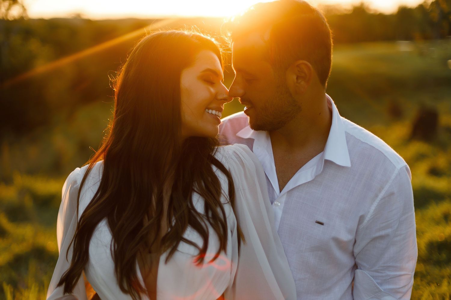 A couple embraces against a warm sunset backdrop in a scenic outdoor setting.