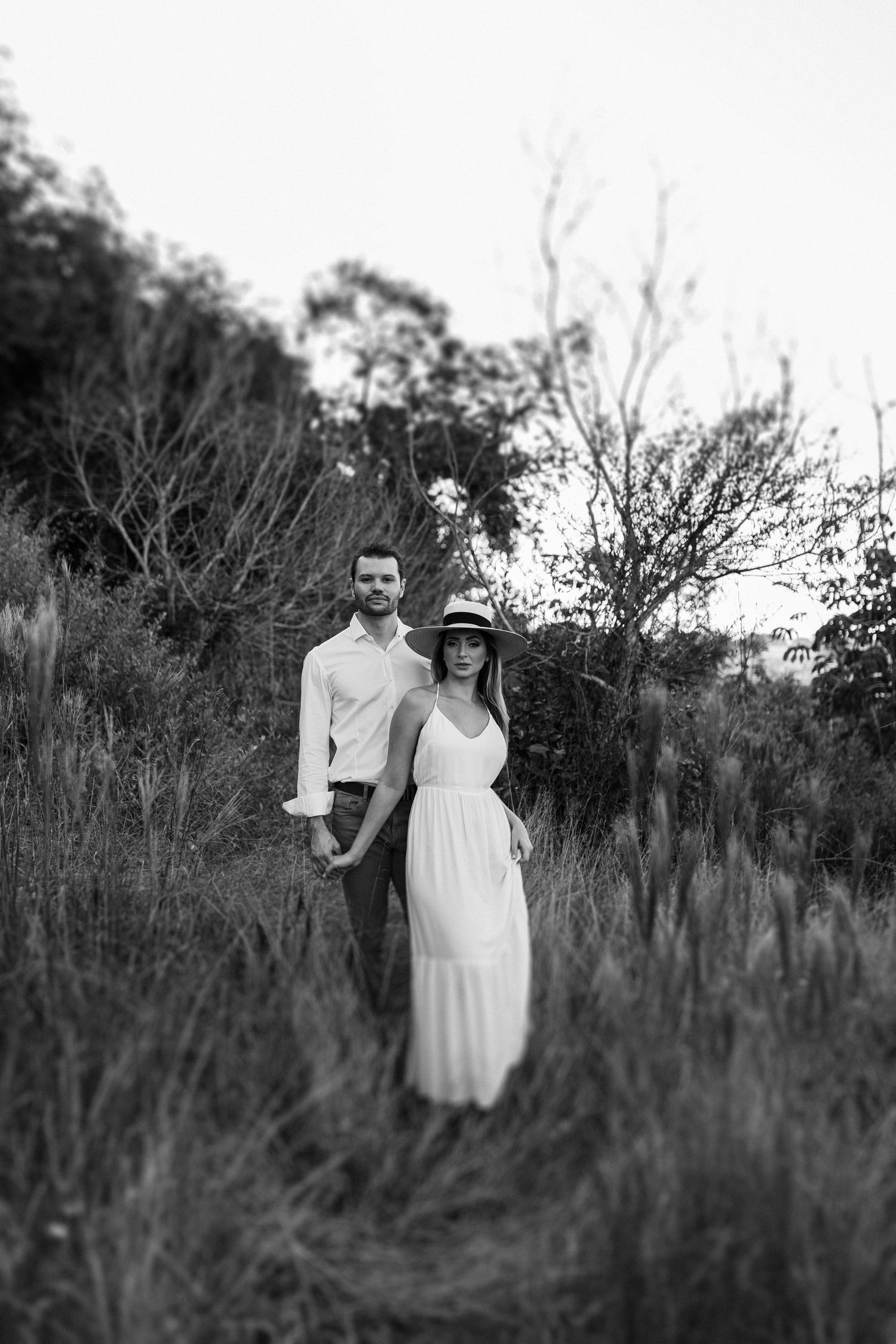Black and white photo of a couple standing together in tall grass at dusk.