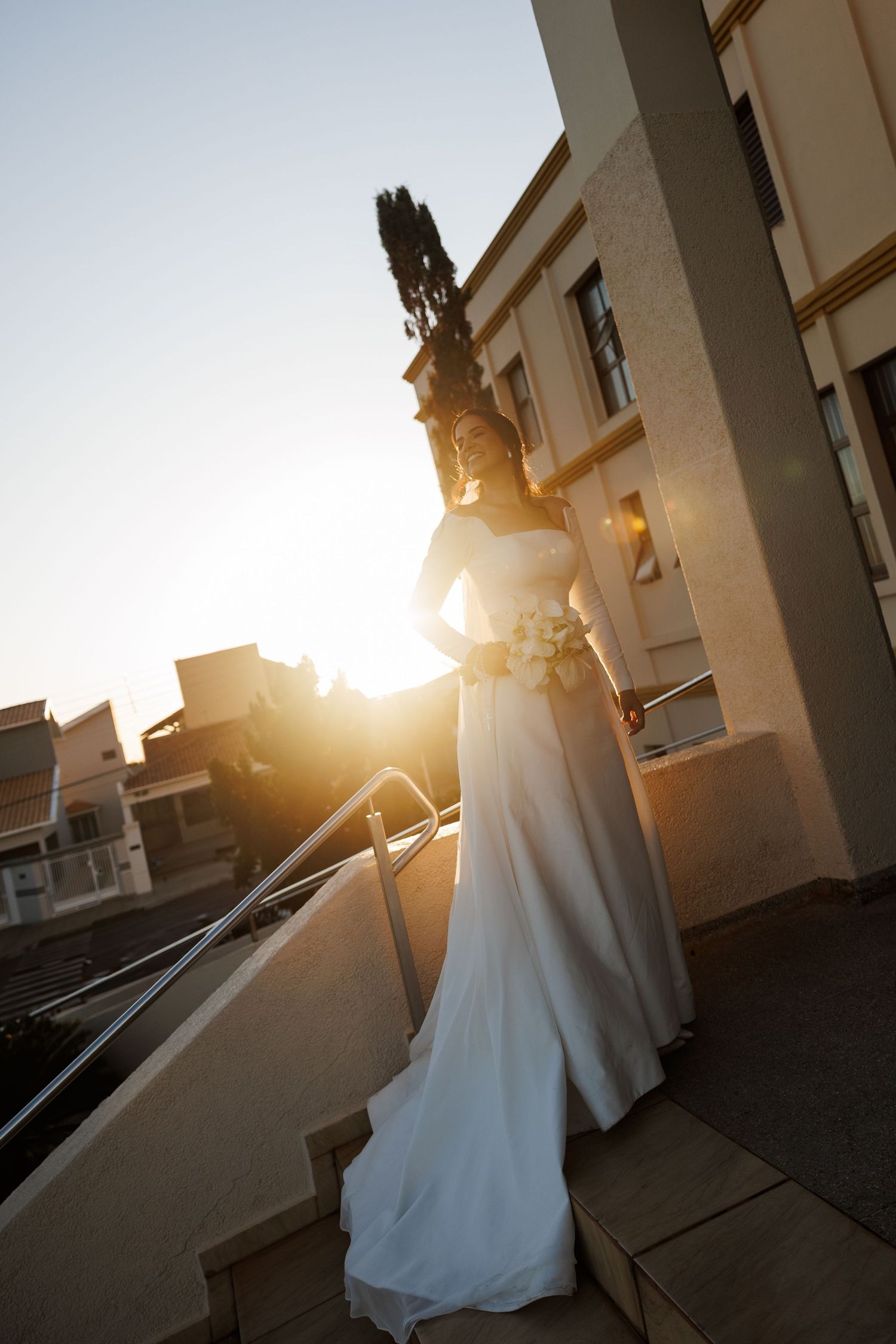 Silhouette of a bride in a flowing white gown against golden sunset light.