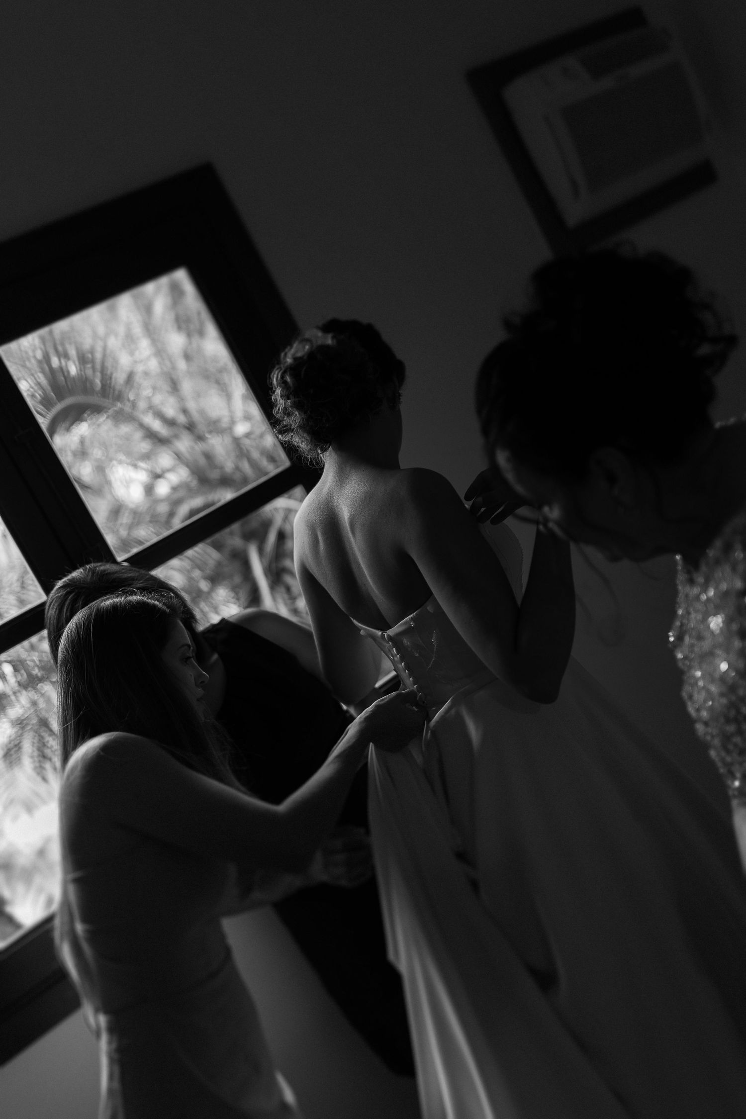 Silhouetted wedding party figures against bright window light in dramatic contrast.