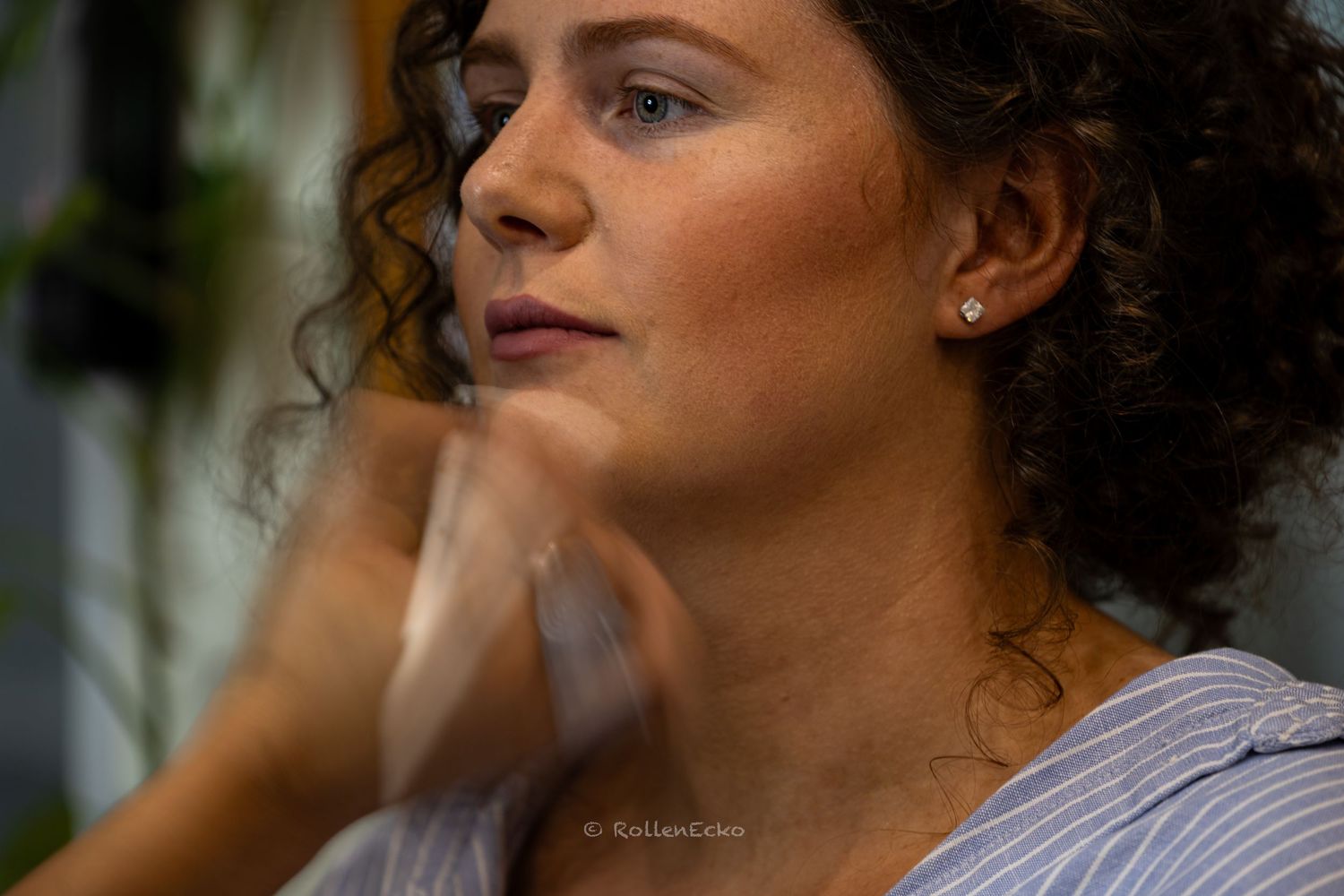 A close up of a woman during a hair and make up session, showing soft brush strokes, natural curls, and a calm expression,